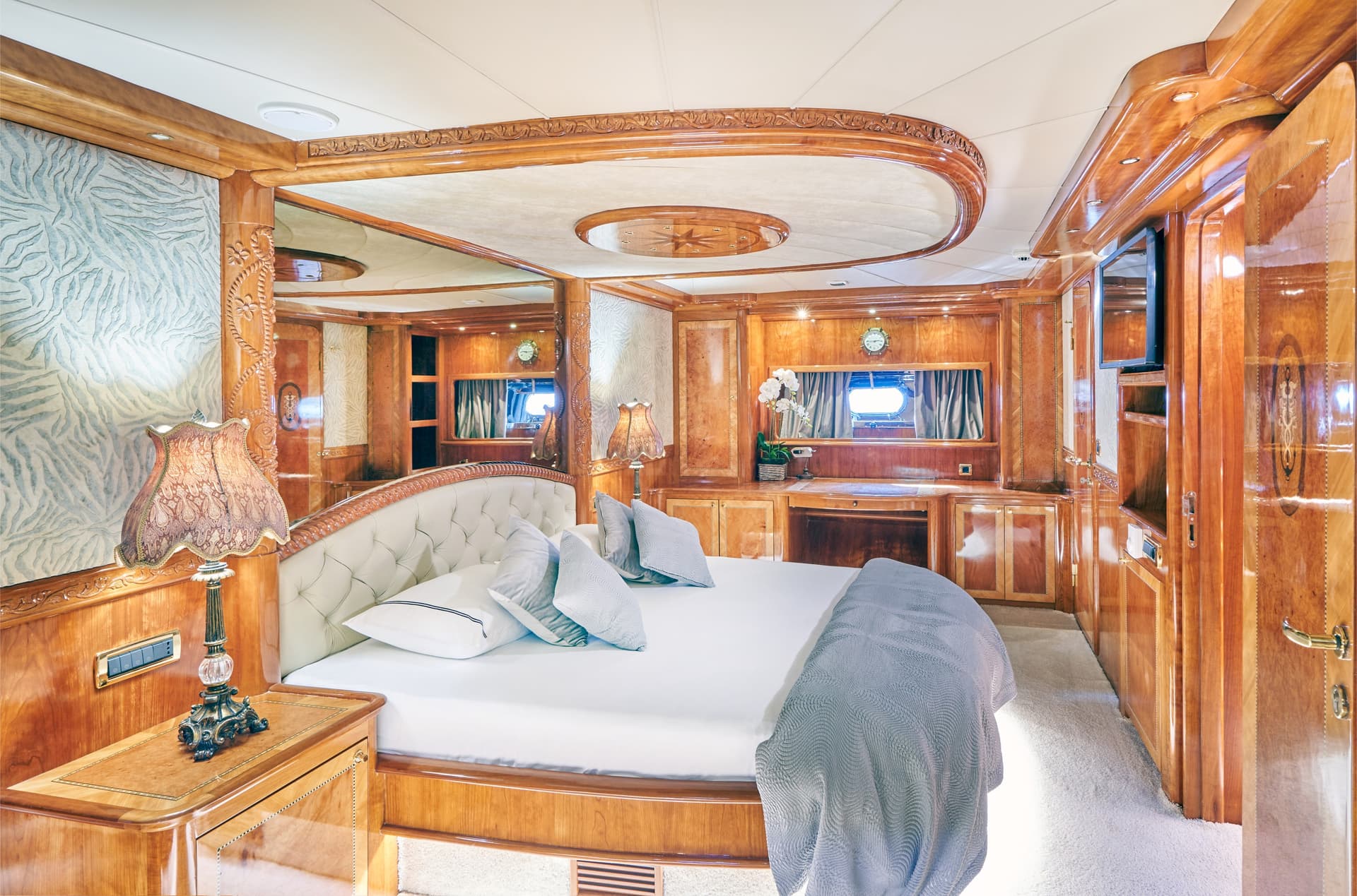 Luxurious yacht cabin bedroom with polished wood paneling and white bedding.