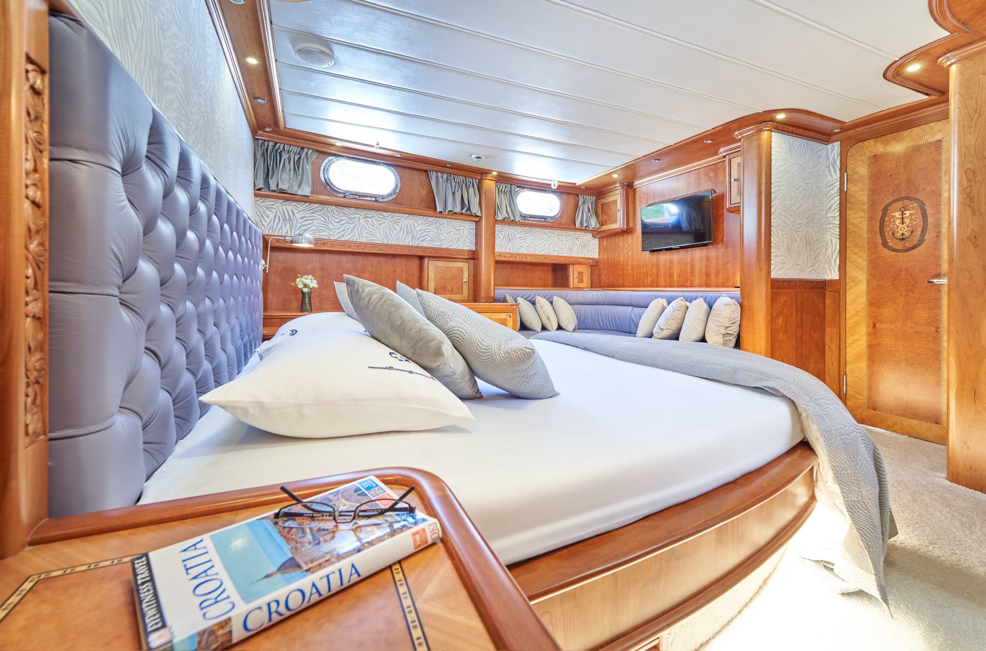 Yacht cabin bedroom with wood paneling, tufted headboard, and Croatia travel guide.