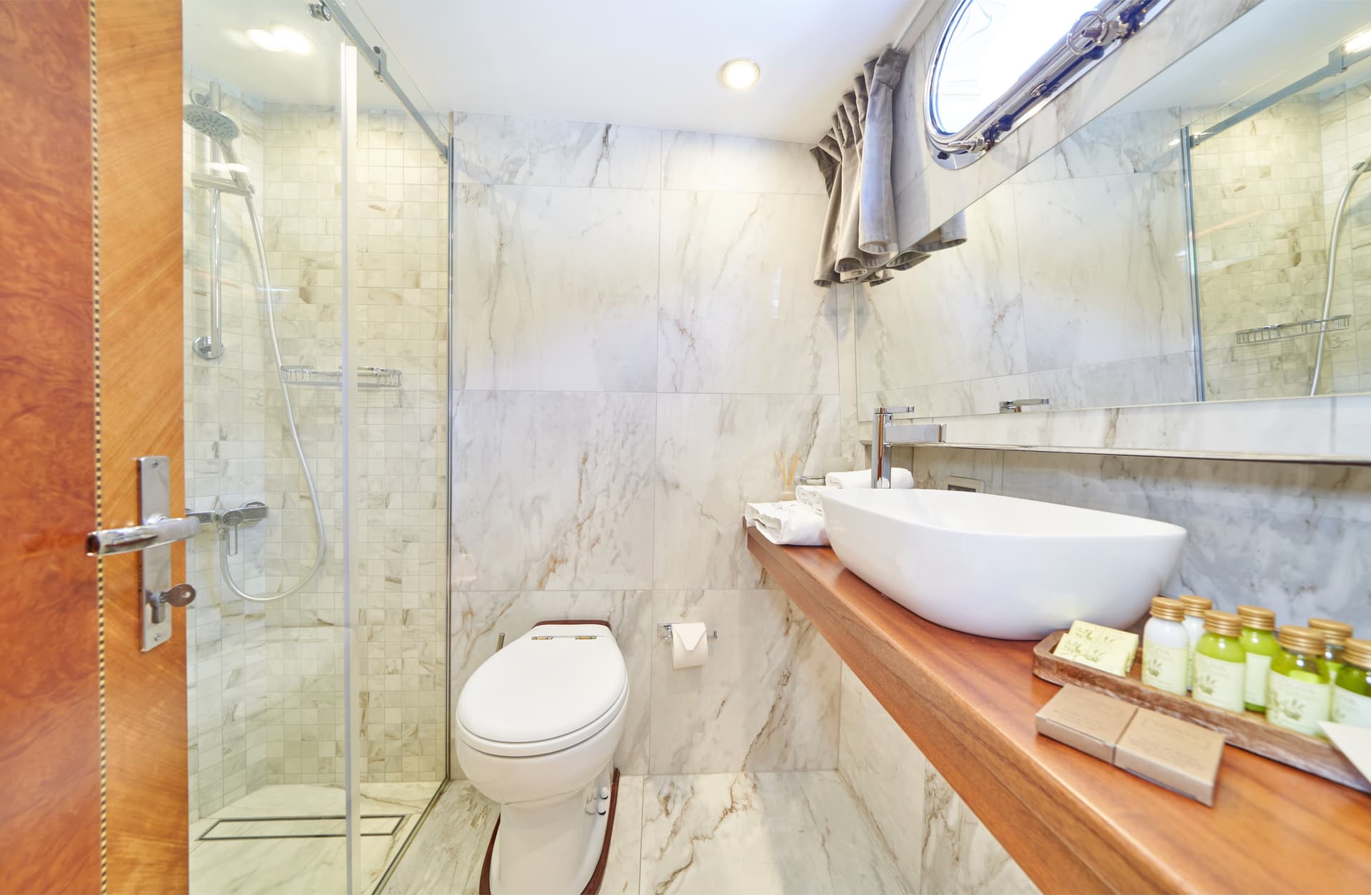 Modern bathroom with white marble walls, vessel sink on wood counter, and glass shower enclosure.