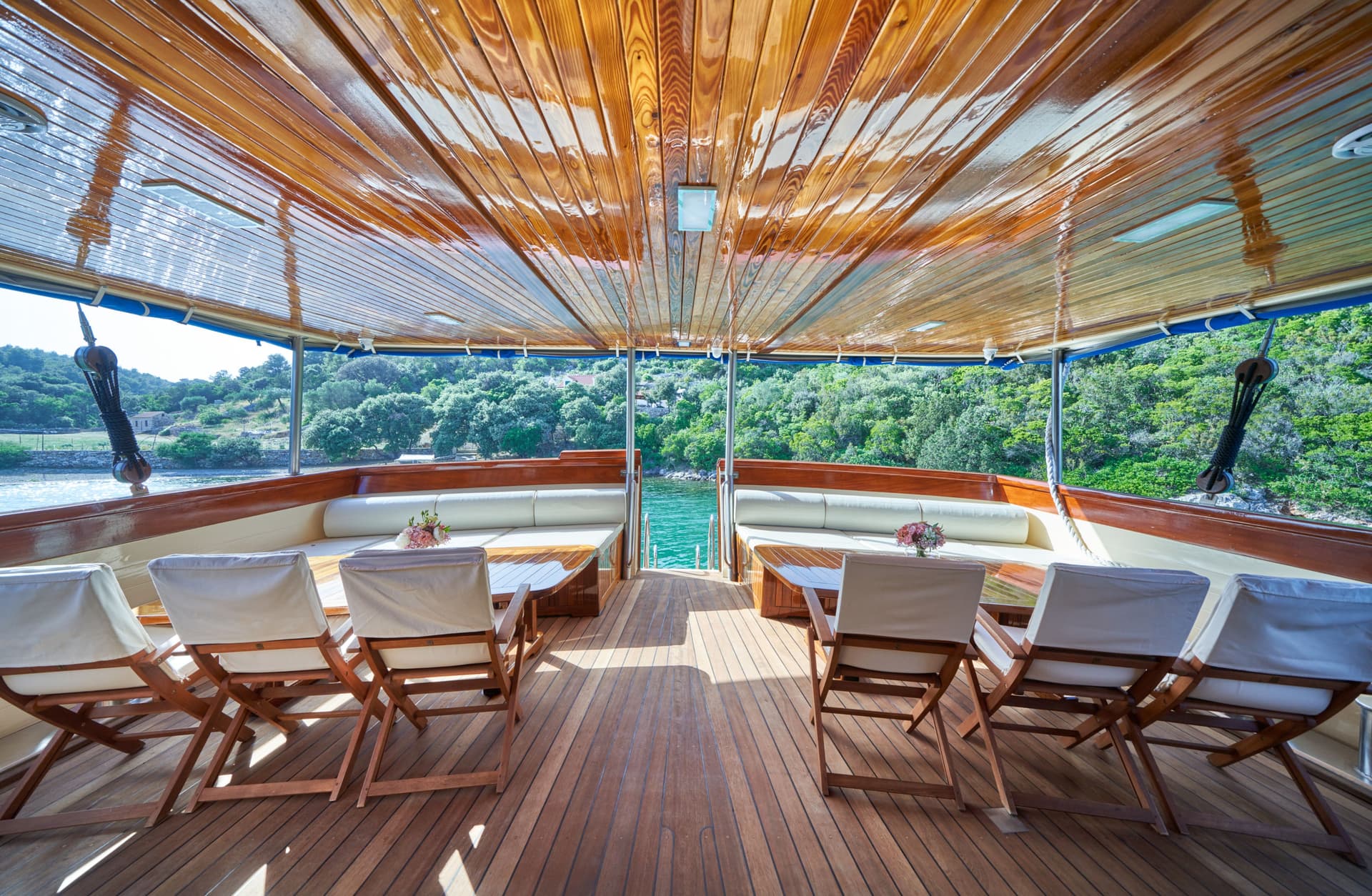 Boat deck with wooden seating looking out at lush green coastline and turquoise water