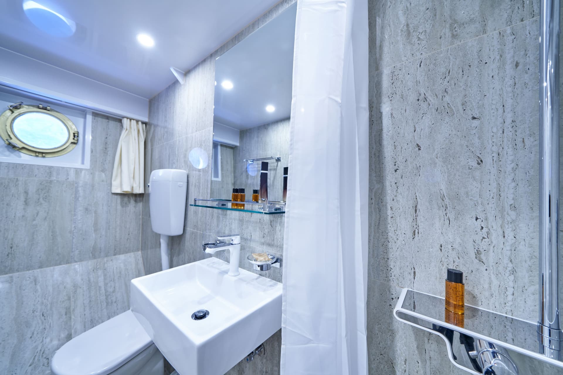 Modern bathroom with stone tile, square sink, and a porthole window suggesting a boat setting.