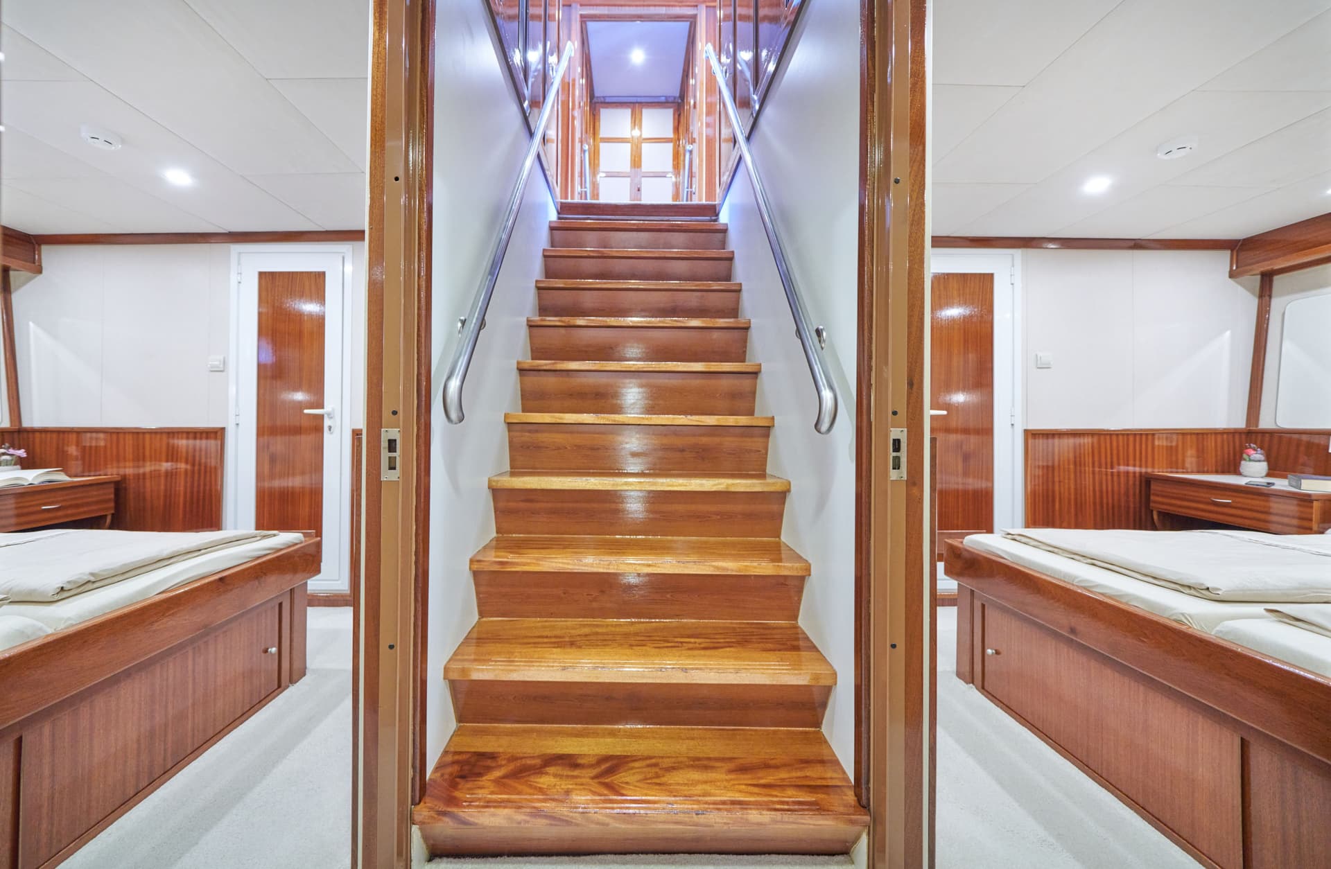 Wooden staircase with metal railing between two cabin bedrooms on a boat or ship.