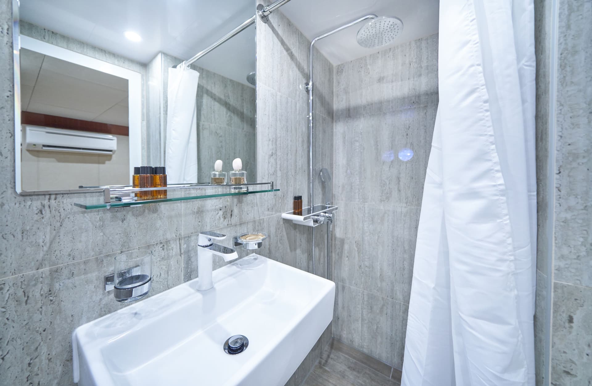 Modern ensuite bathroom with white sink, chrome fixtures, mirror, and grey tiled walls.