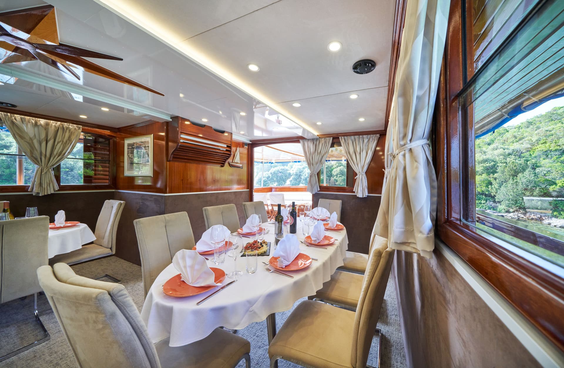 Indoor restaurant dining area on a boat with wood paneling and view of green coastline.