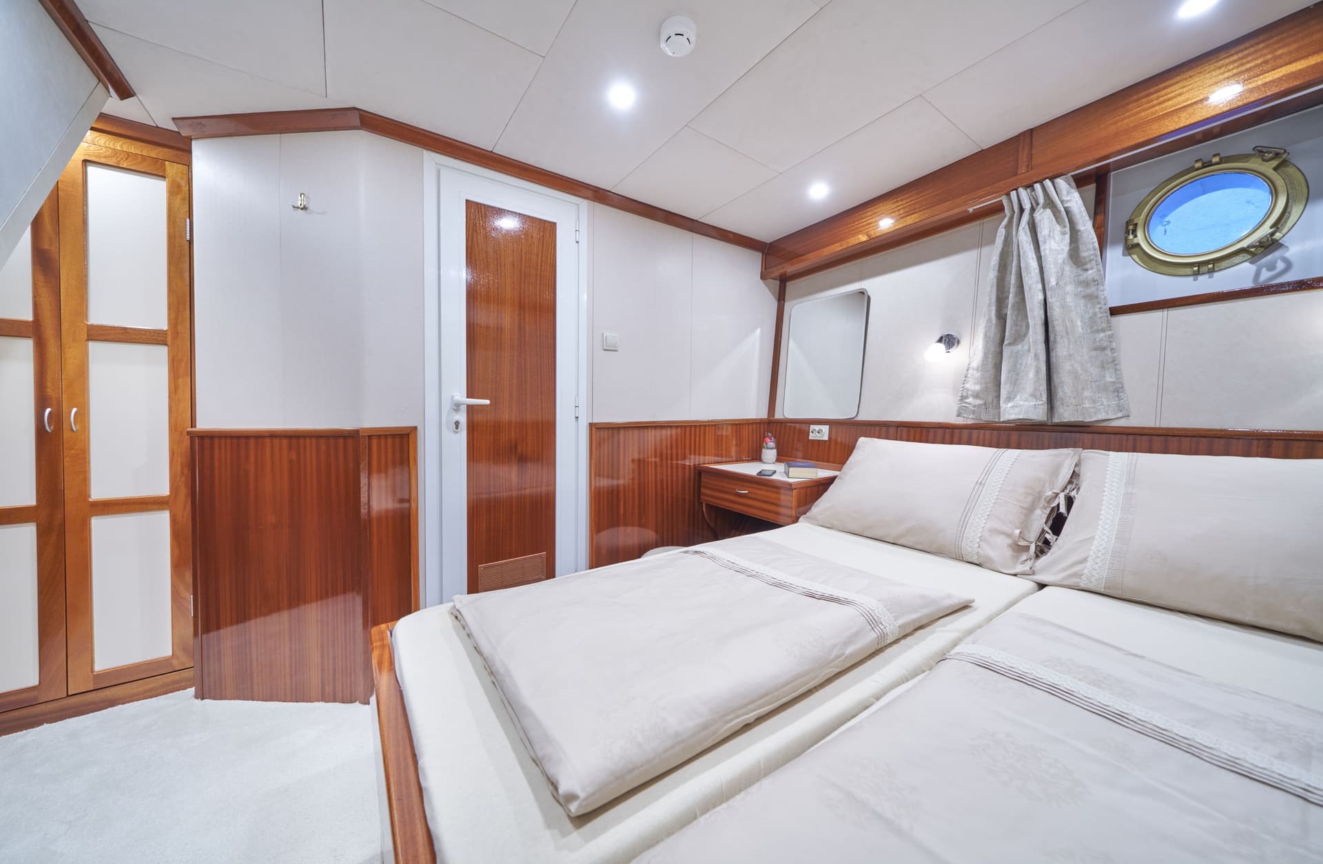 Master cabin bedroom on a boat with twin beds, wood trim, and a round porthole window.