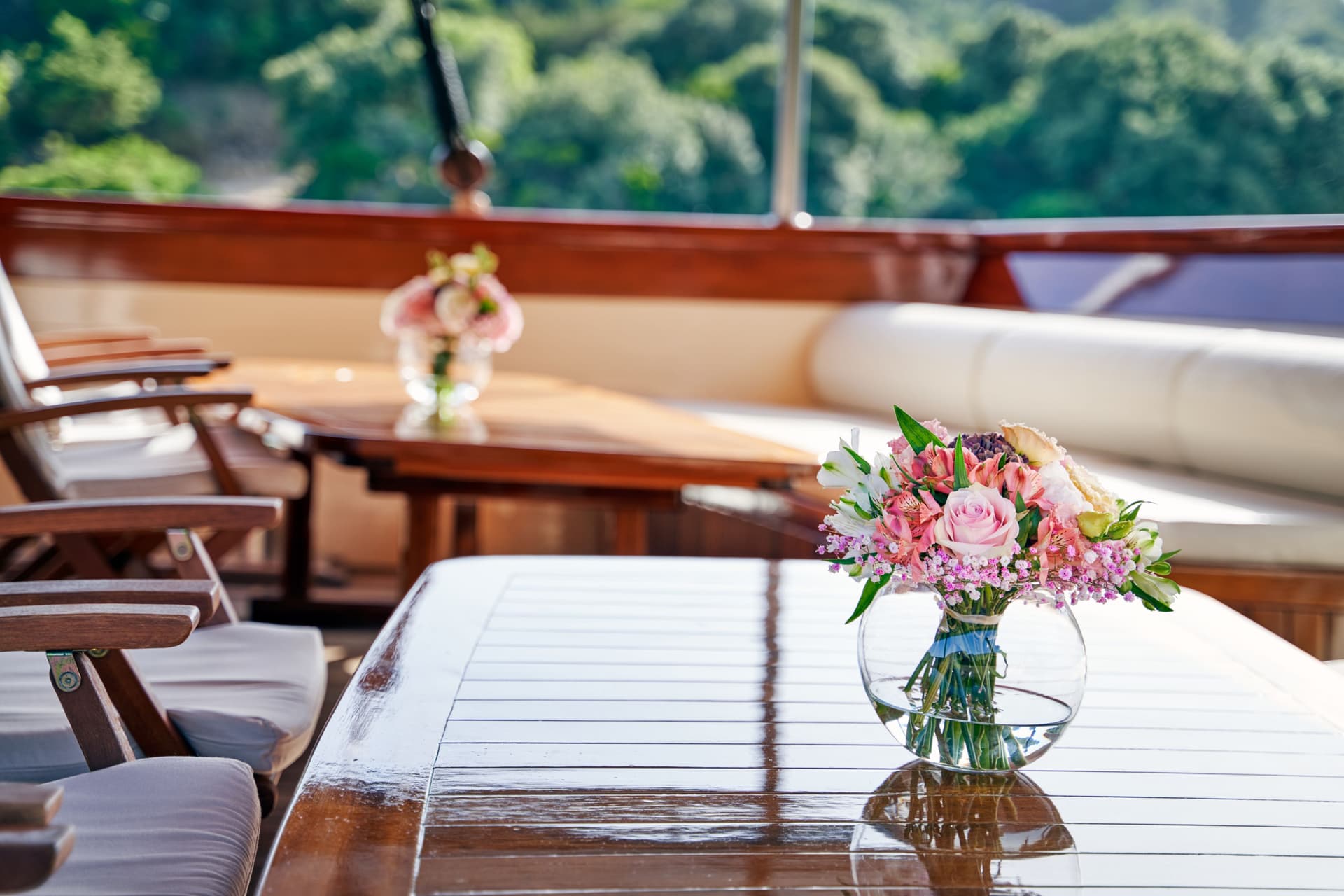 Outdoor dining area on a boat with a floral centerpiece and lush greenery background.