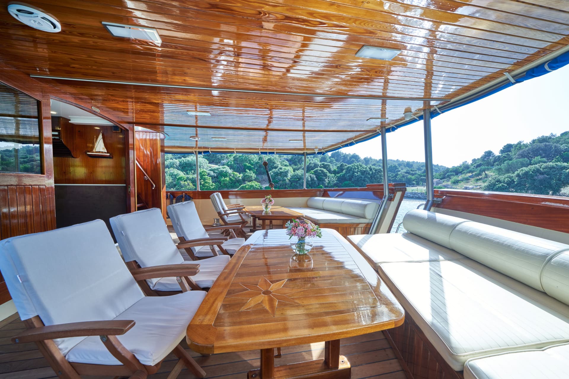 Outdoor seating area on a wooden boat deck overlooking a lush, green coastline.