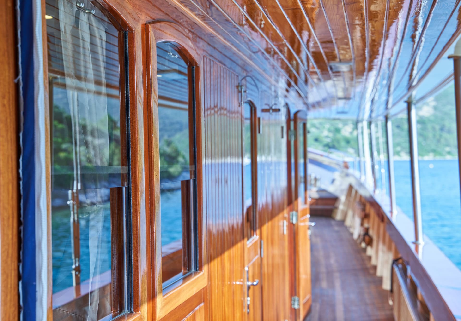 Glossy wooden cabin exterior with windows reflecting blue water and green coastline.
