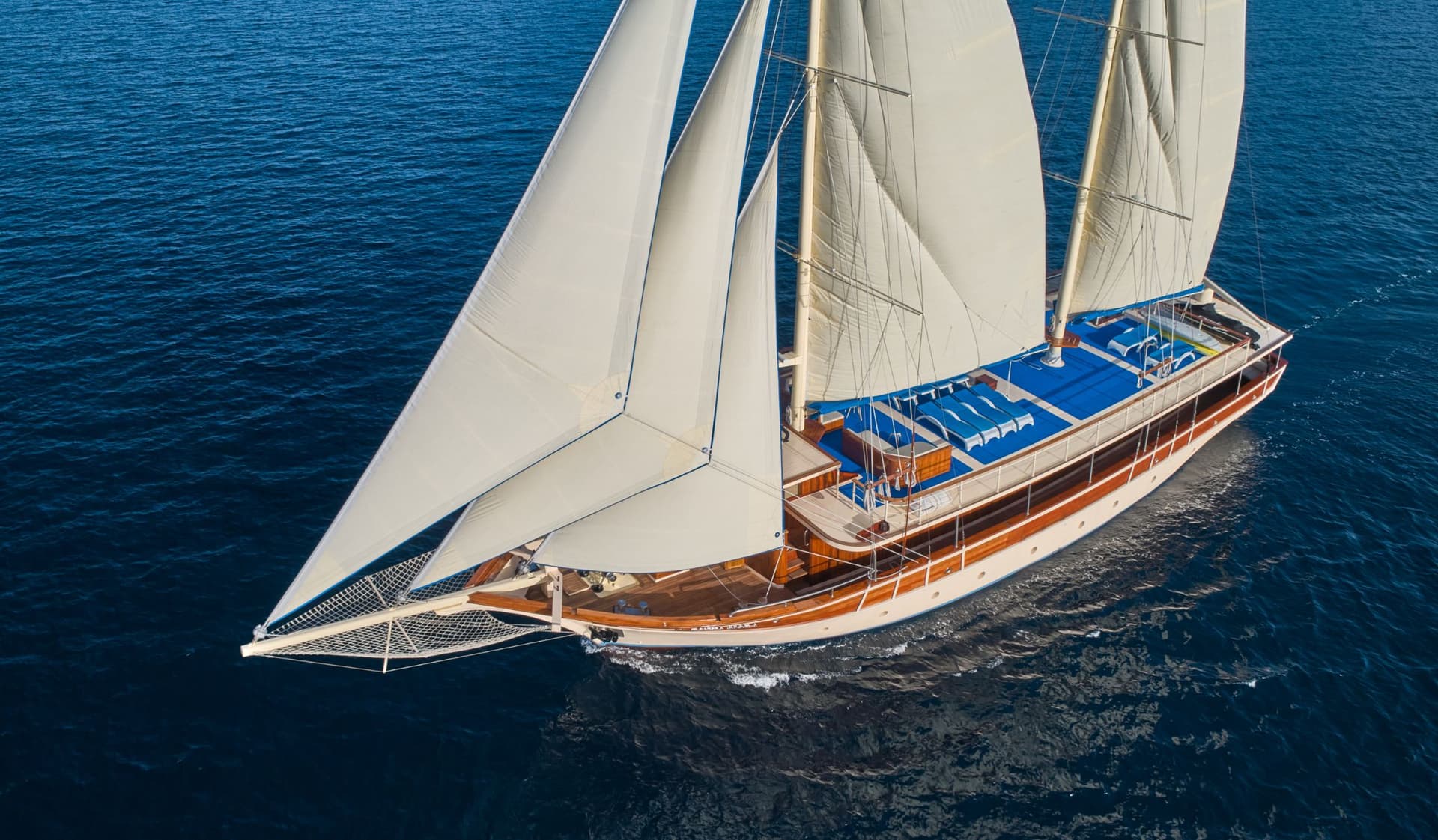 Wooden sailing yacht with white sails cruising on deep blue coastal waters, aerial view