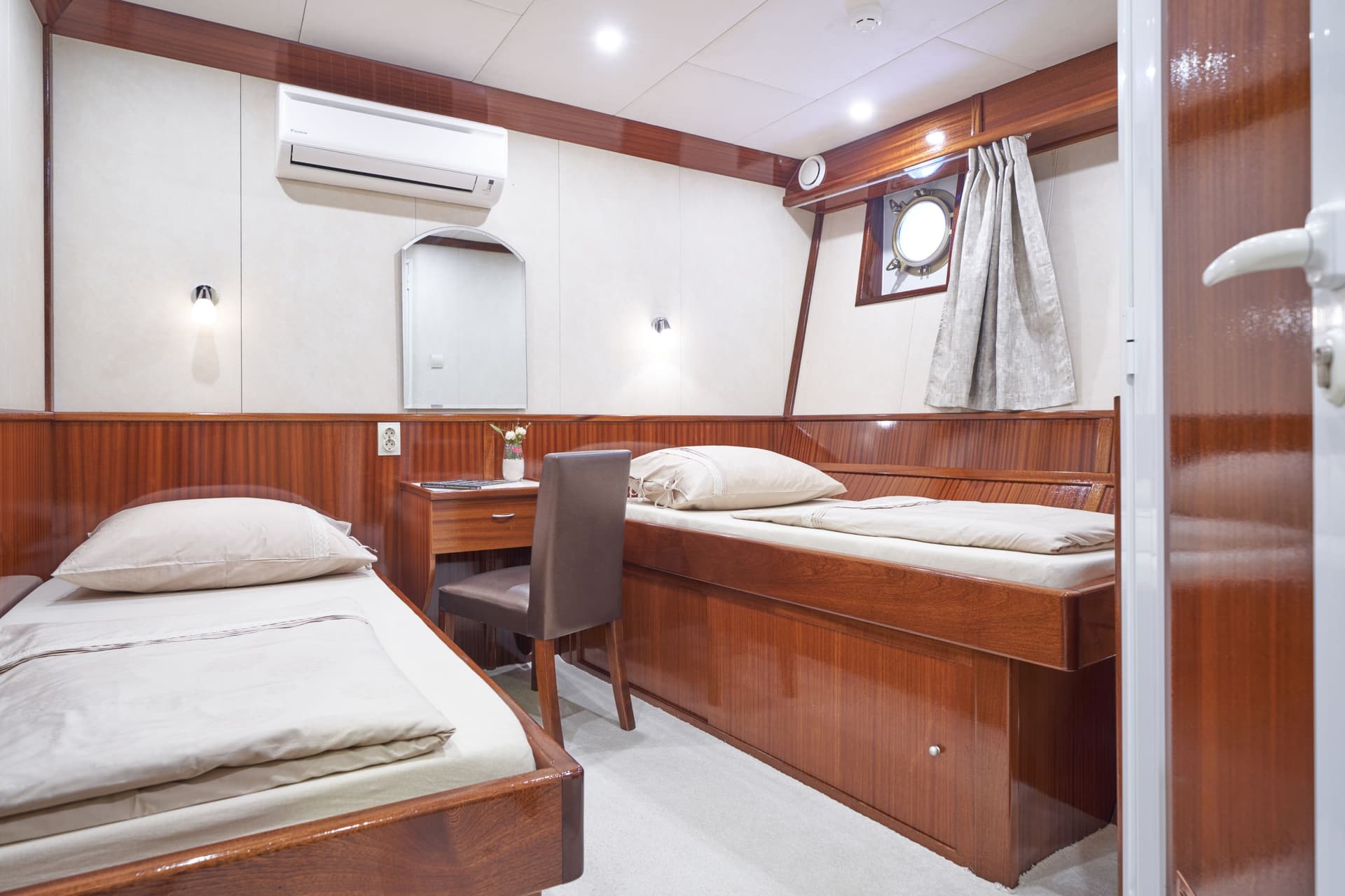 Twin cabin interior on a boat with wood paneling, white walls, and a round porthole window.