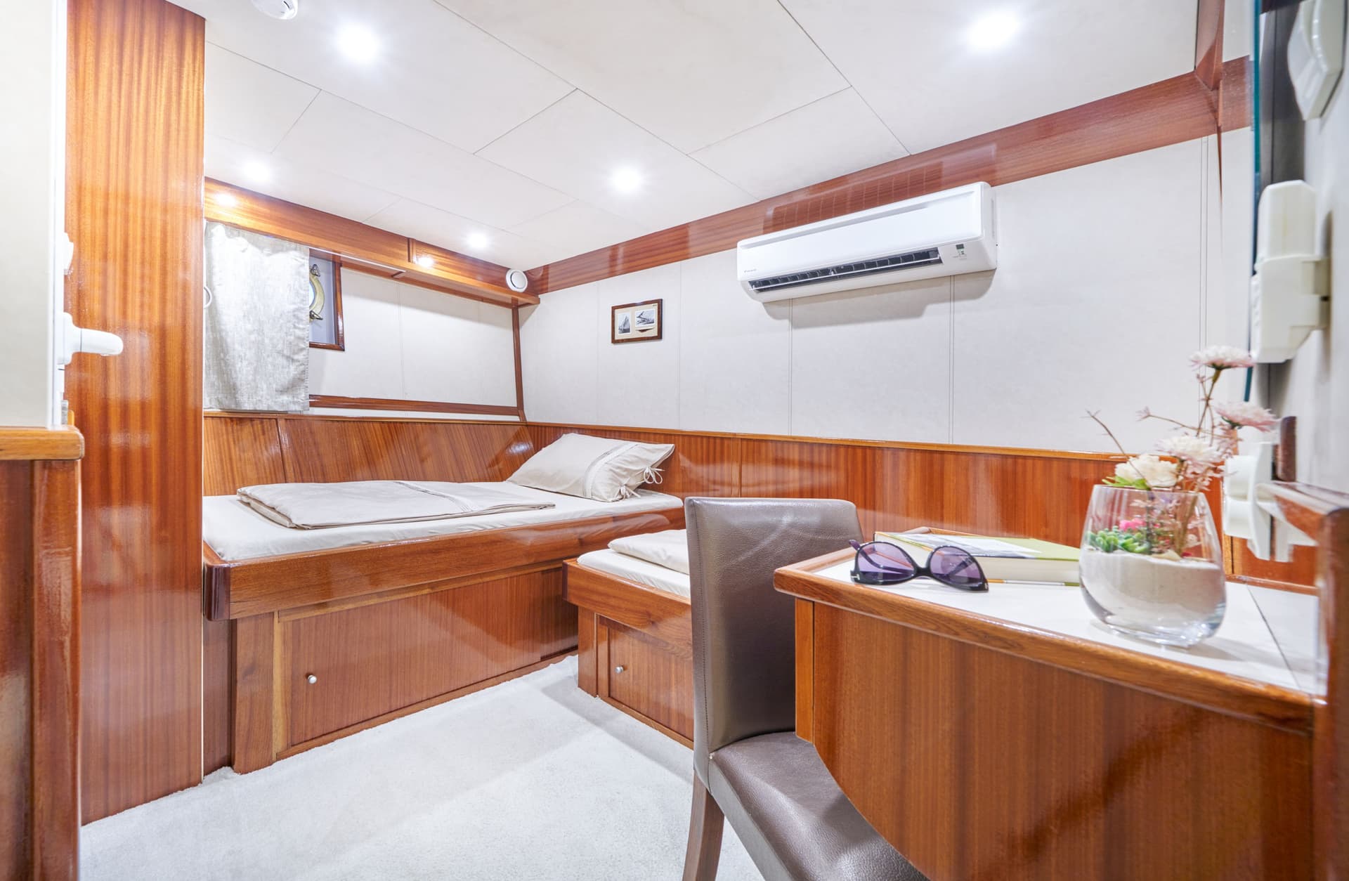 Cabin interior with twin beds, wood paneling, air conditioner, and desk area.