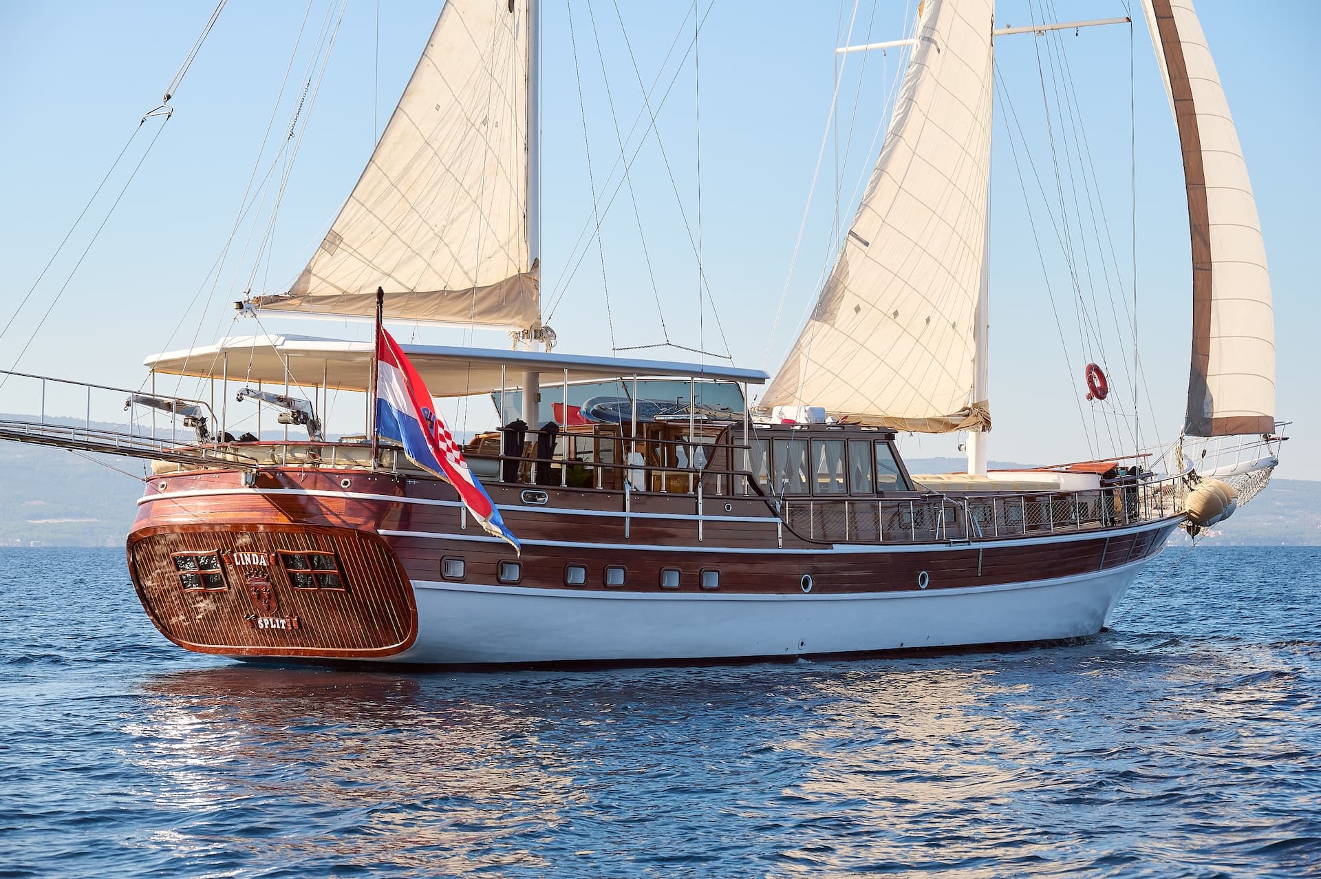 Wooden sailboat Linda from Split sailing with Croatian flag on blue sea near coast.