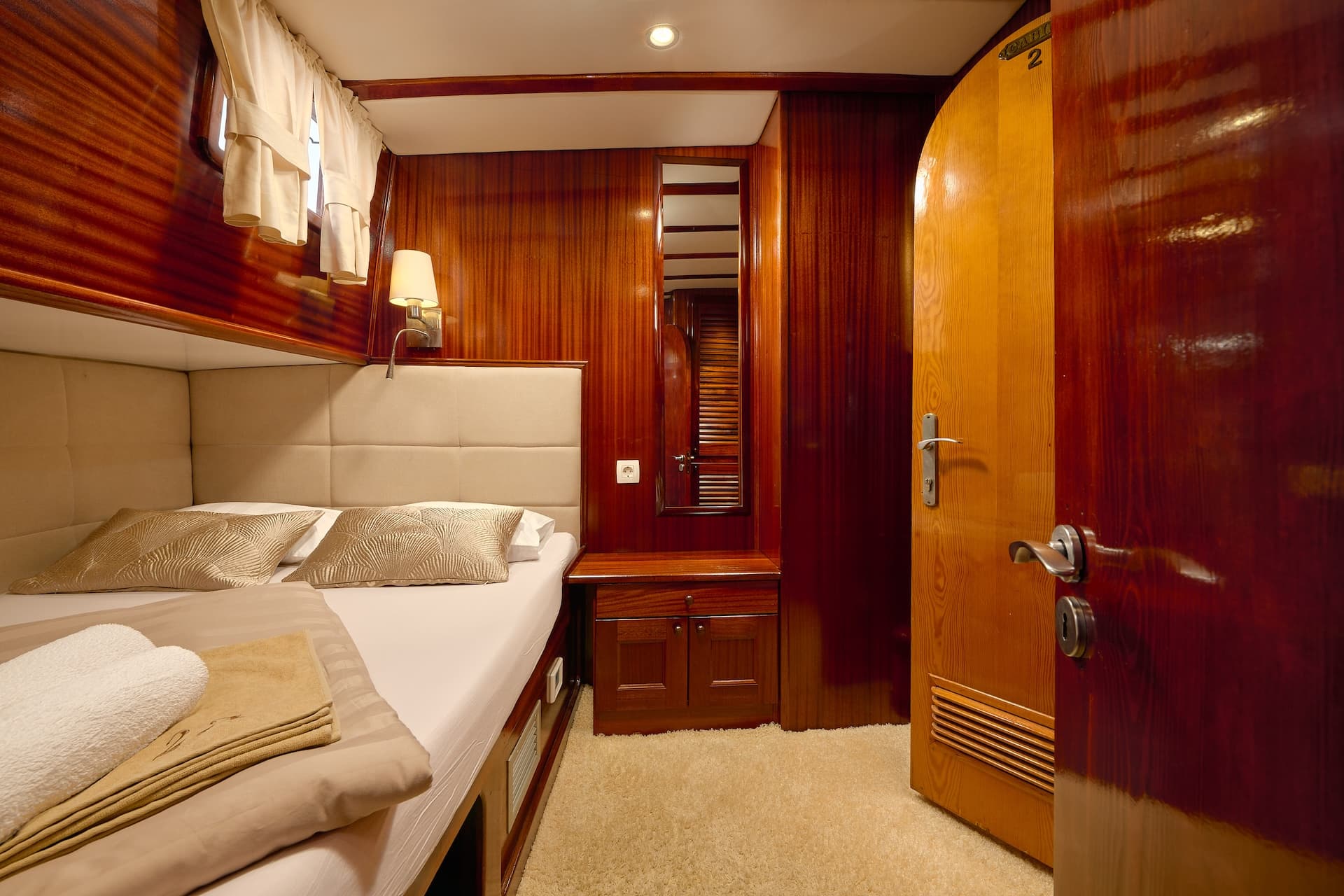Cabin interior with wood paneling, double bed, and beige carpet, likely on a boat.