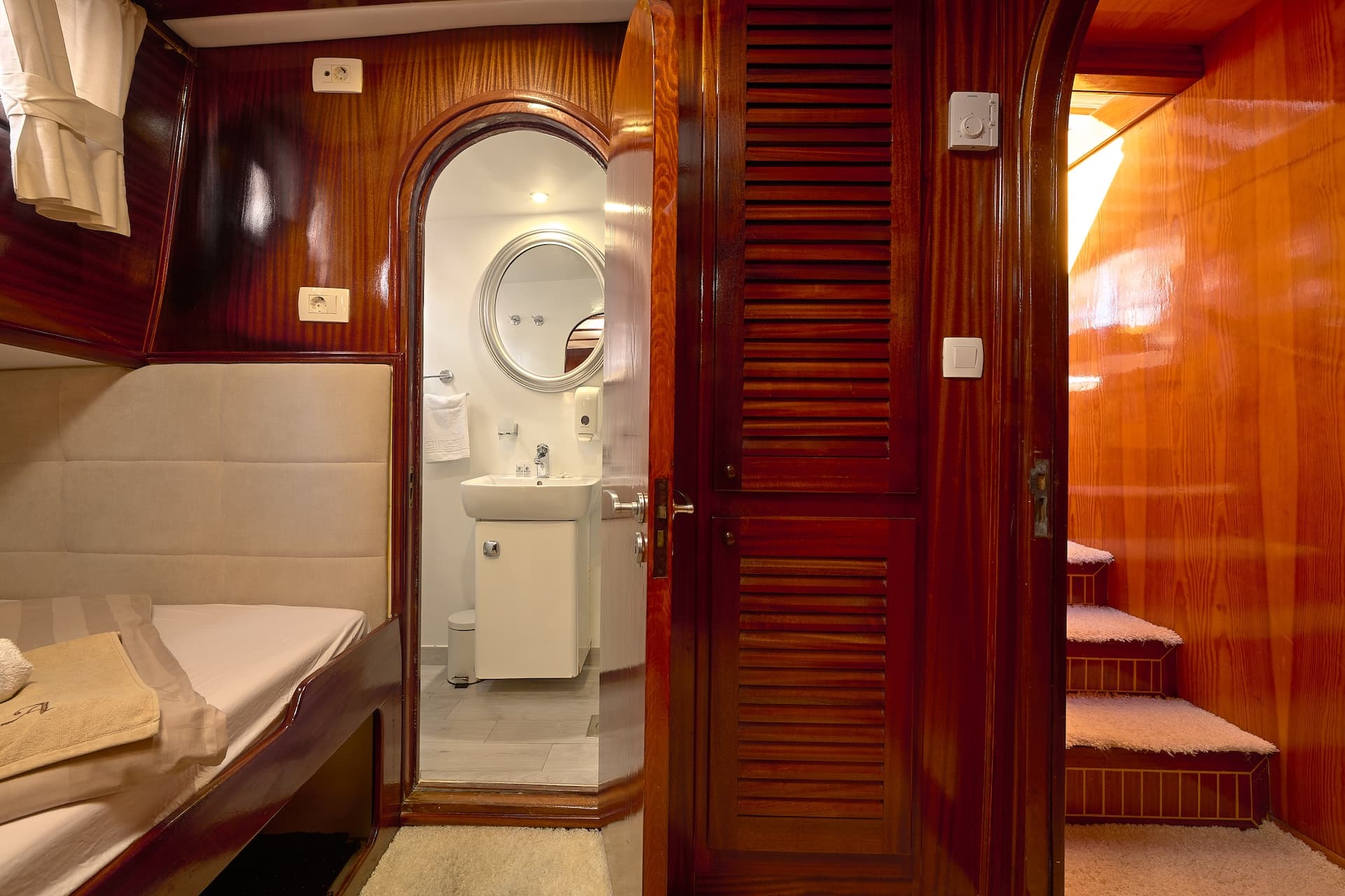 Cabin interior with wood paneling, bed, ensuite bathroom, and stairs leading up.