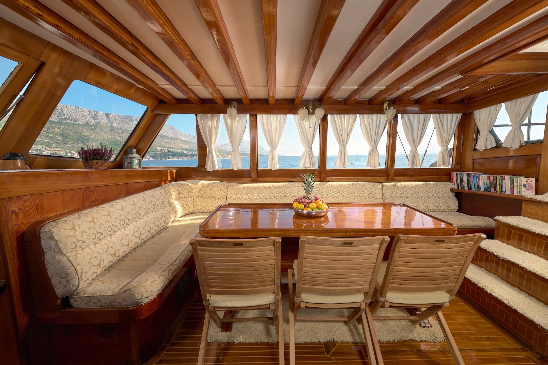 Wooden boat interior dining area with fruit bowl, facing mountains and sea view