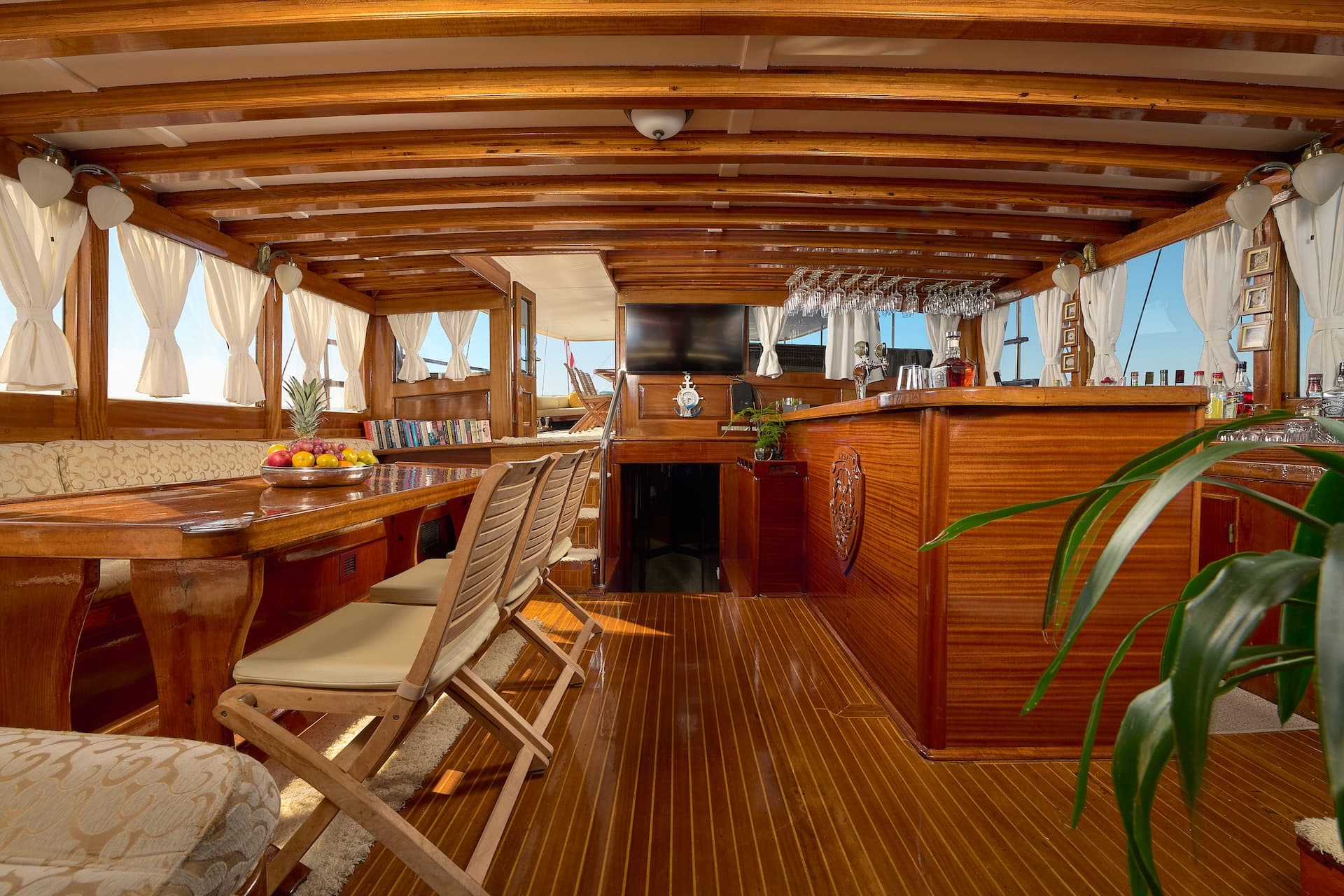 Interior salon of a wooden boat with a dining table, bar, and bright windows.