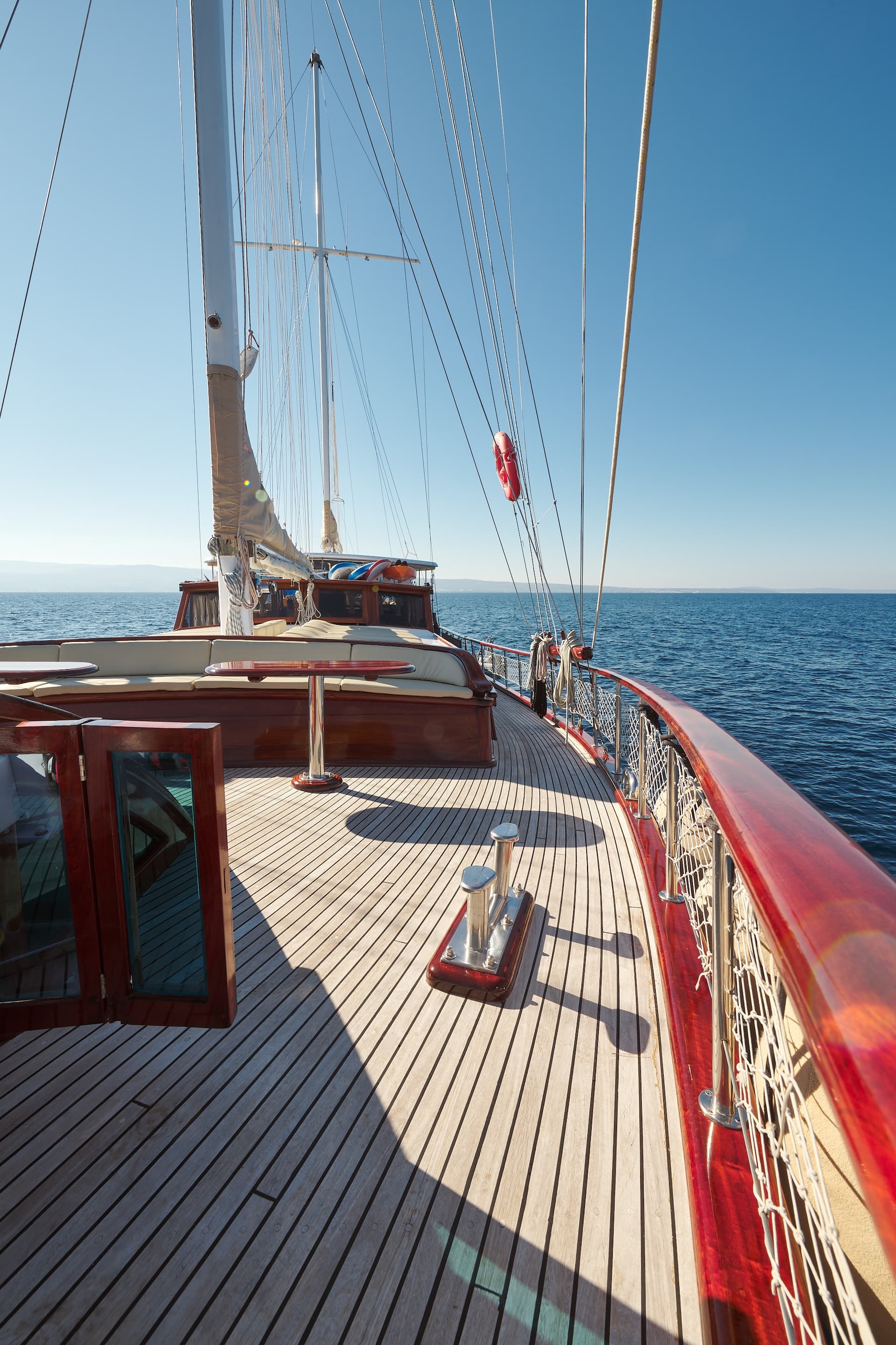Wooden deck of a sailboat with rigging and blue sea visible under clear sky