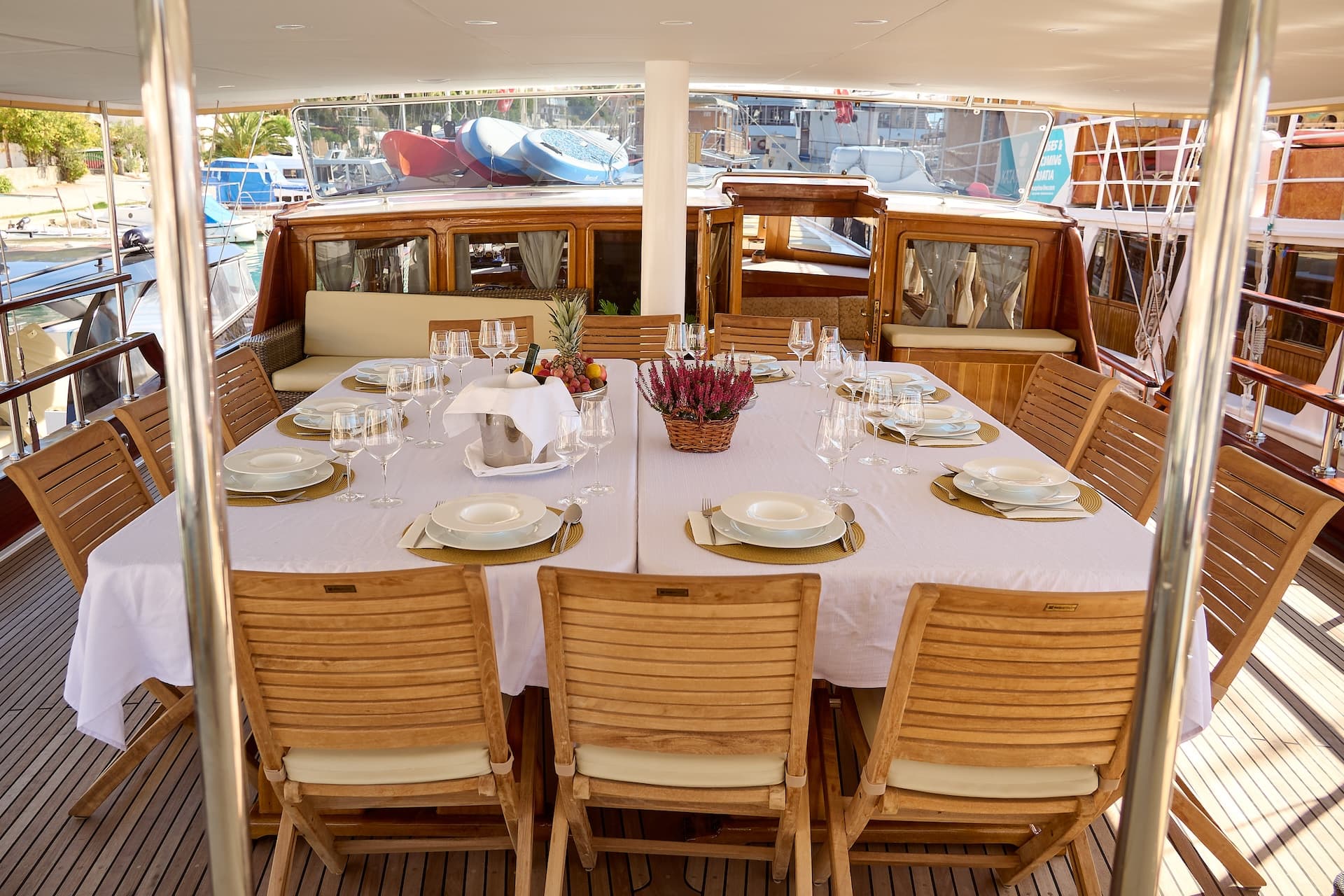 Outdoor dining table set on a yacht deck near a harbor with other boats.