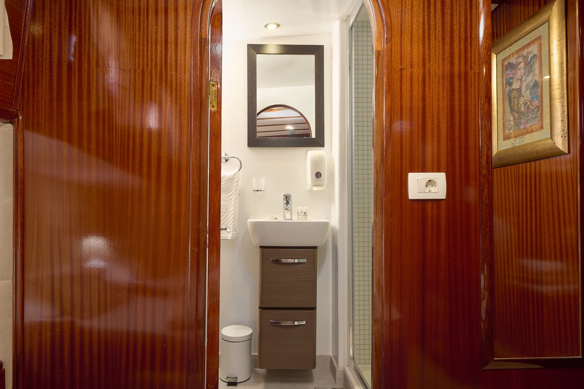 Small bathroom vanity with sink, mirror, and glossy wood paneling, likely on a boat.