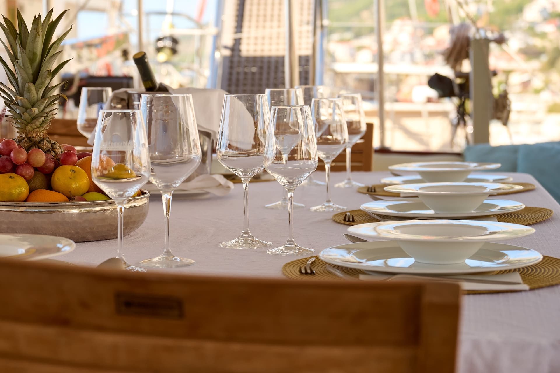 Set dining table with wine glasses and fruit bowl on a boat deck overlooking a town.