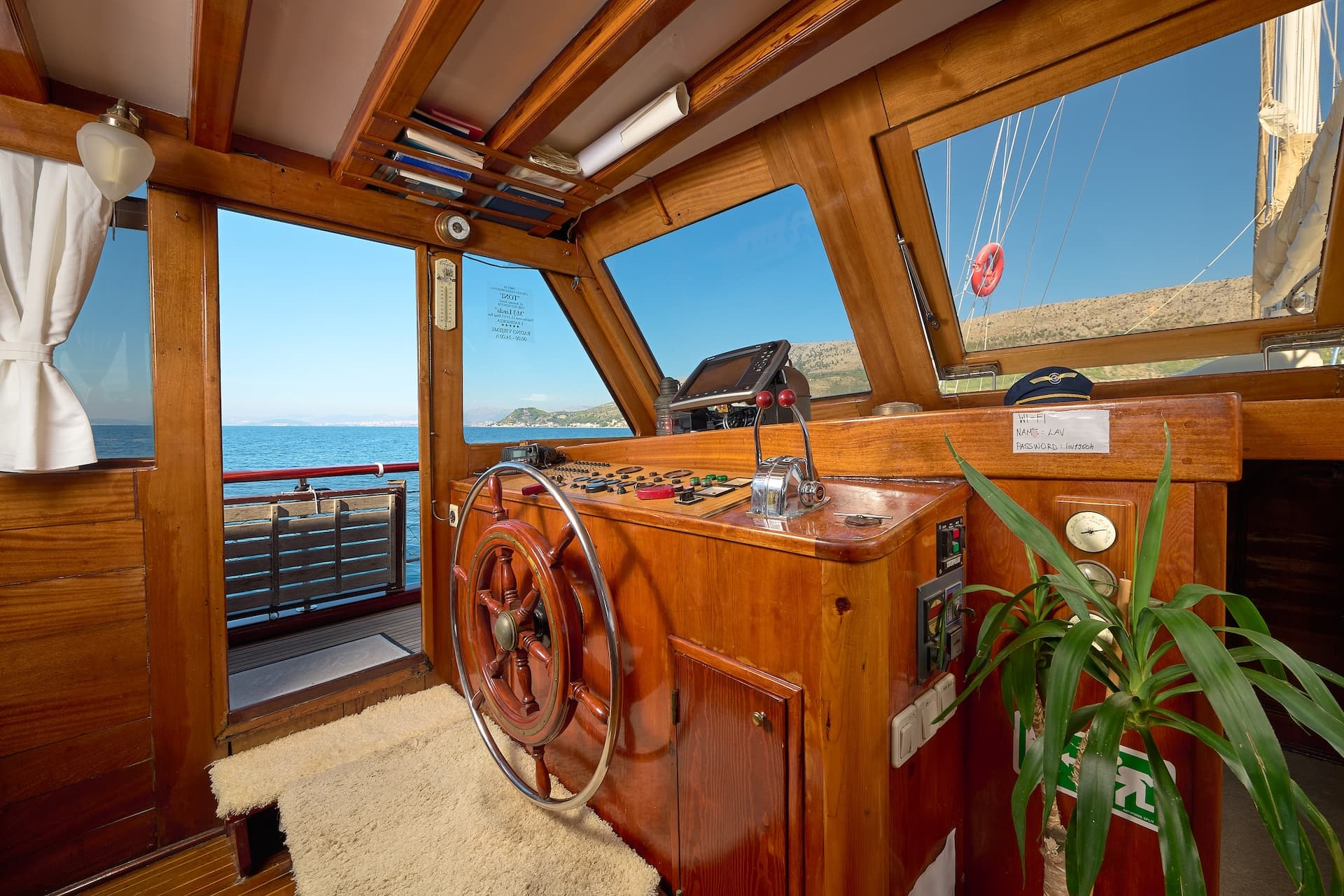 Boat helm station with wooden paneling and view of blue sea and distant coastline