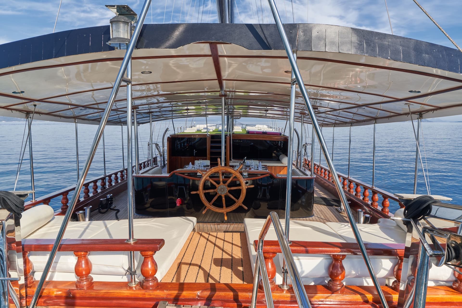 Wooden steering wheel on deck of yacht with sun canopy over blue sea.