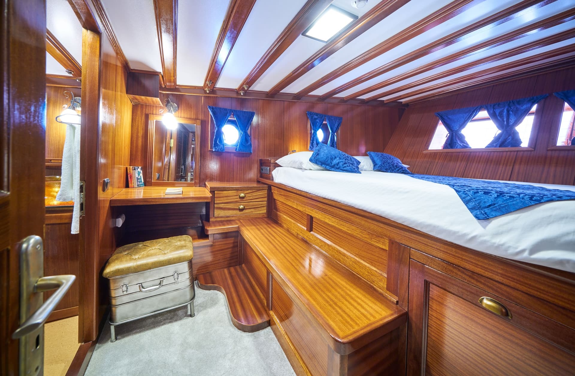 Cabin interior with polished wood paneling, built-in bed with blue accents, and porthole windows.