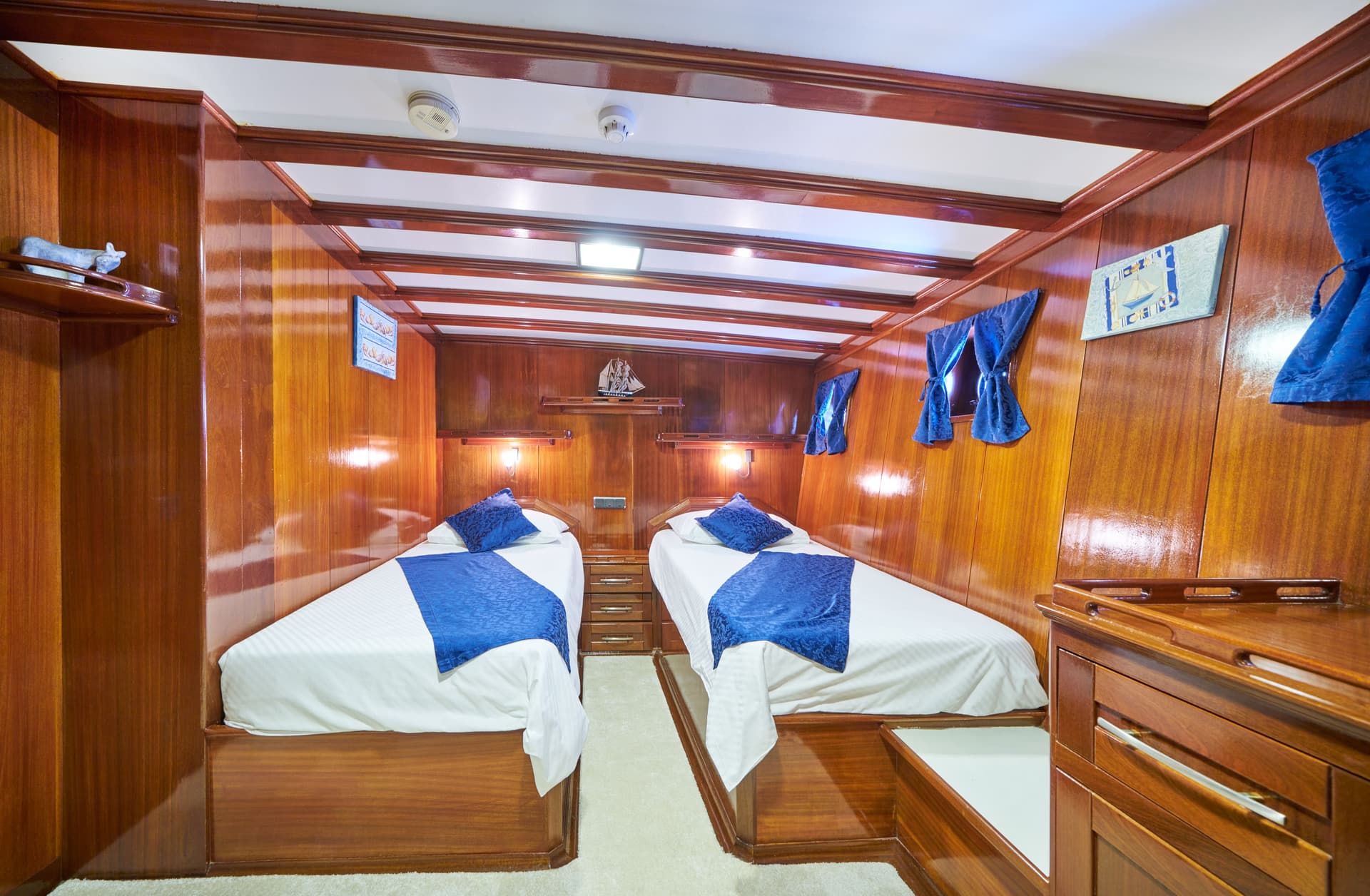 Twin cabin interior with glossy wood paneling, white bedding, and blue accents on a boat.