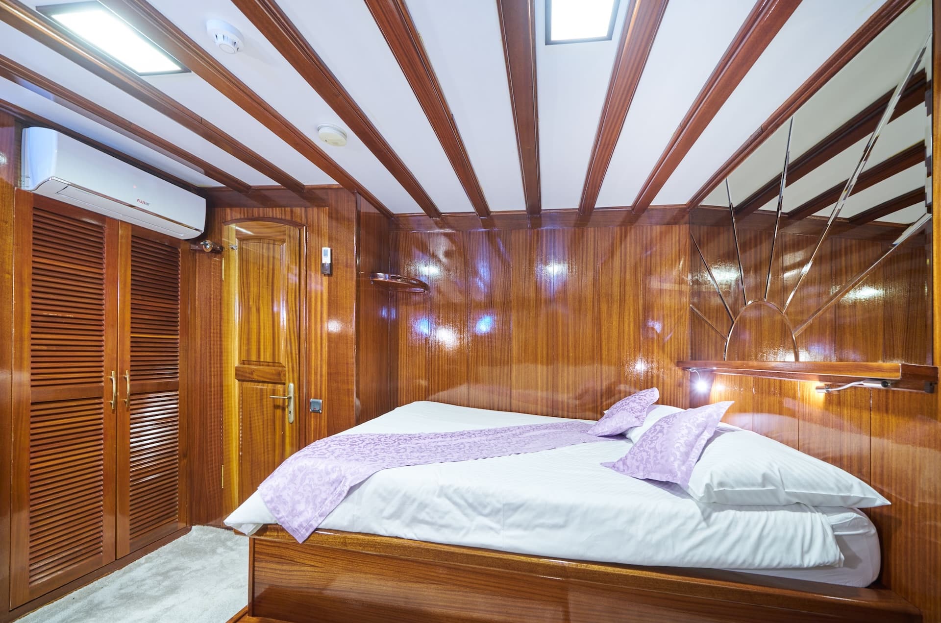 Double cabin bedroom with polished wood paneling, white bedding, and purple accents on a boat.