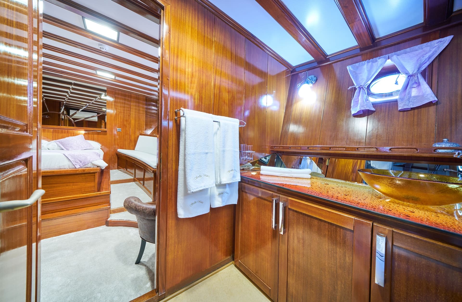 Yacht ensuite bathroom with glossy wood paneling and view into a bedroom cabin.