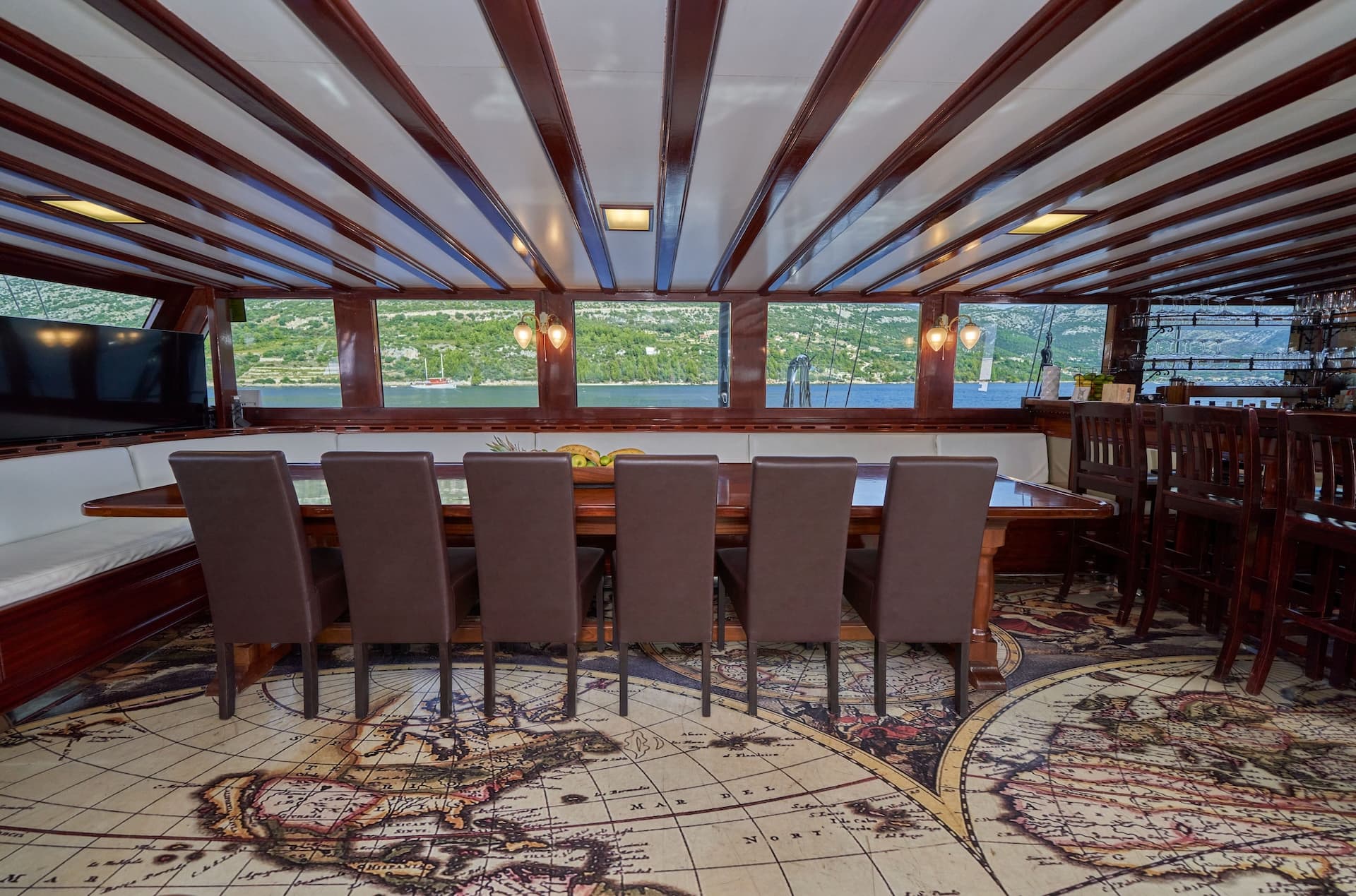 Dining area inside a boat with world map flooring and view of green coastline.