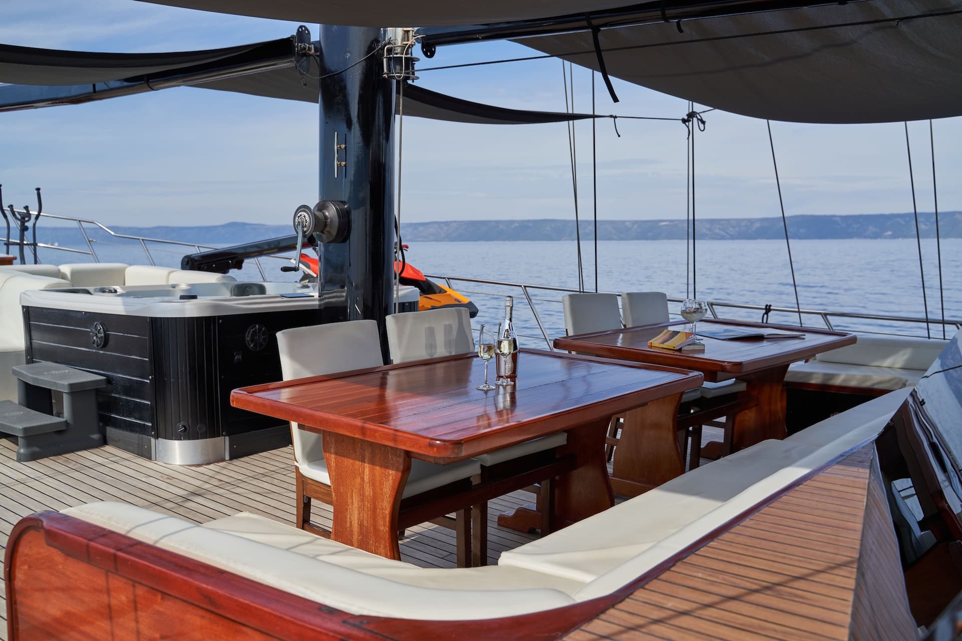 Yacht deck with wooden tables, hot tub, and sea view of distant coastline