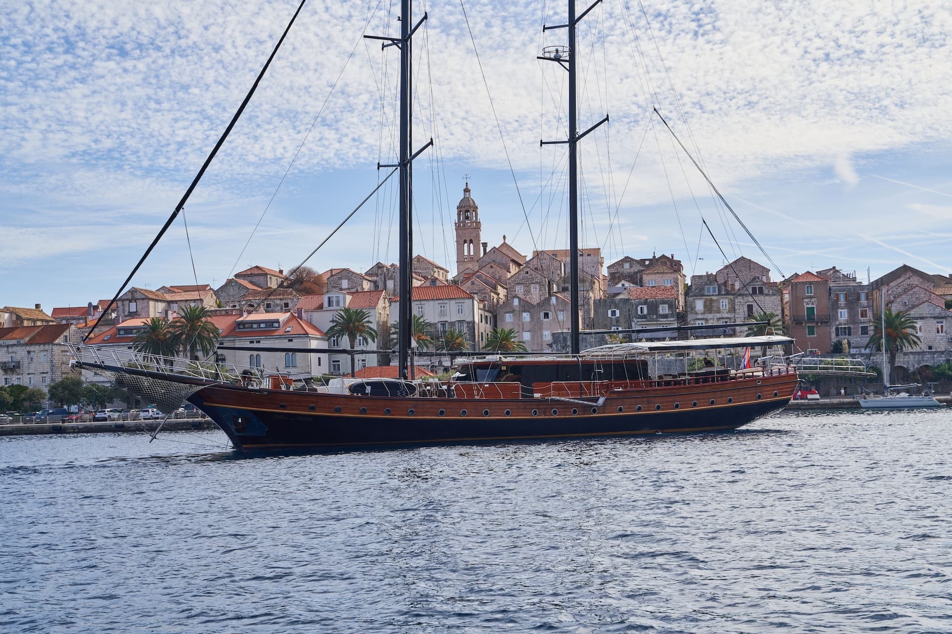 Wooden sailboat Stella Maris on water with historic Croatian town and bell tower background.