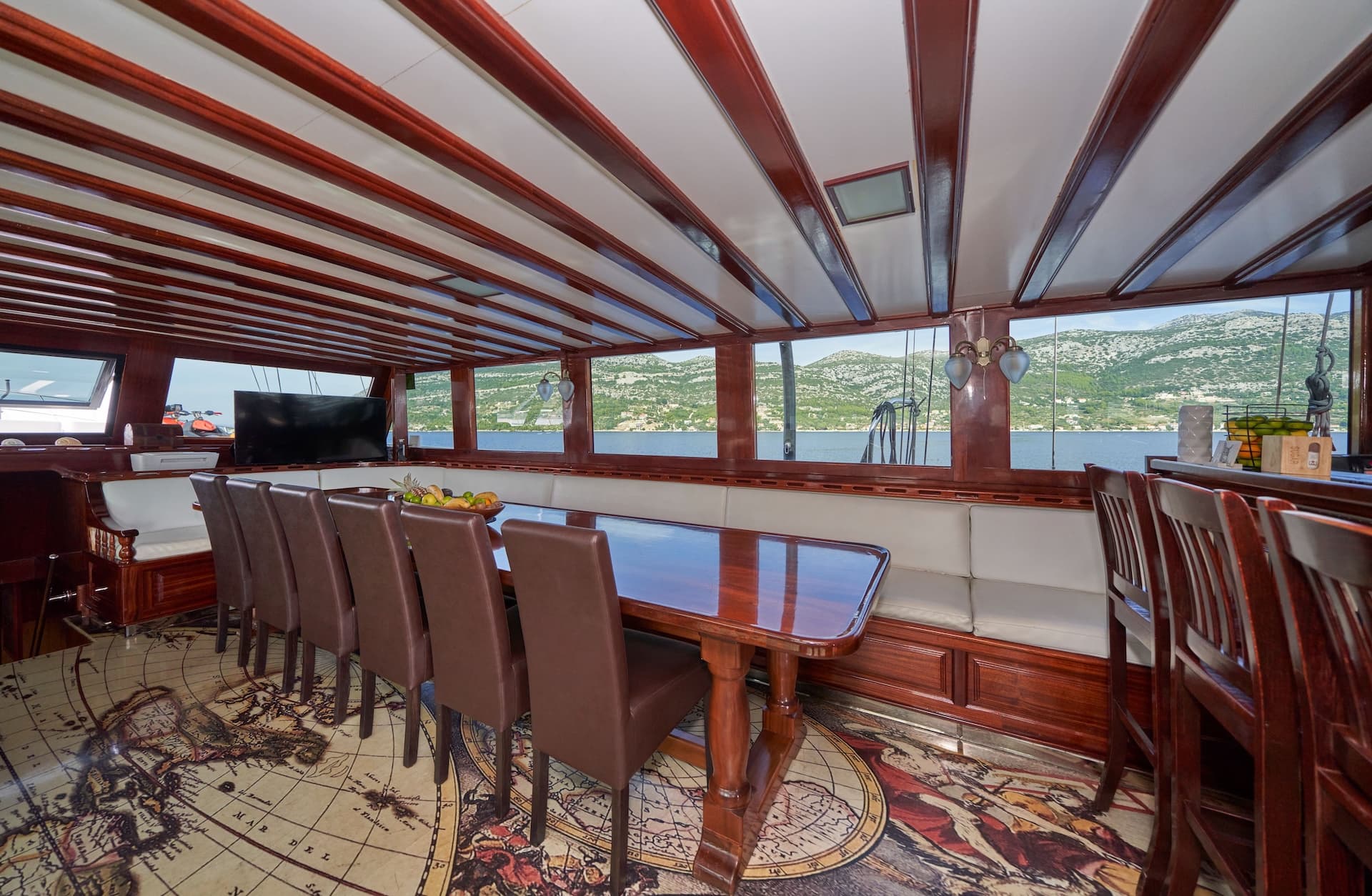Interior dining area of Stella Maris boat with map floor and view of green coastline.