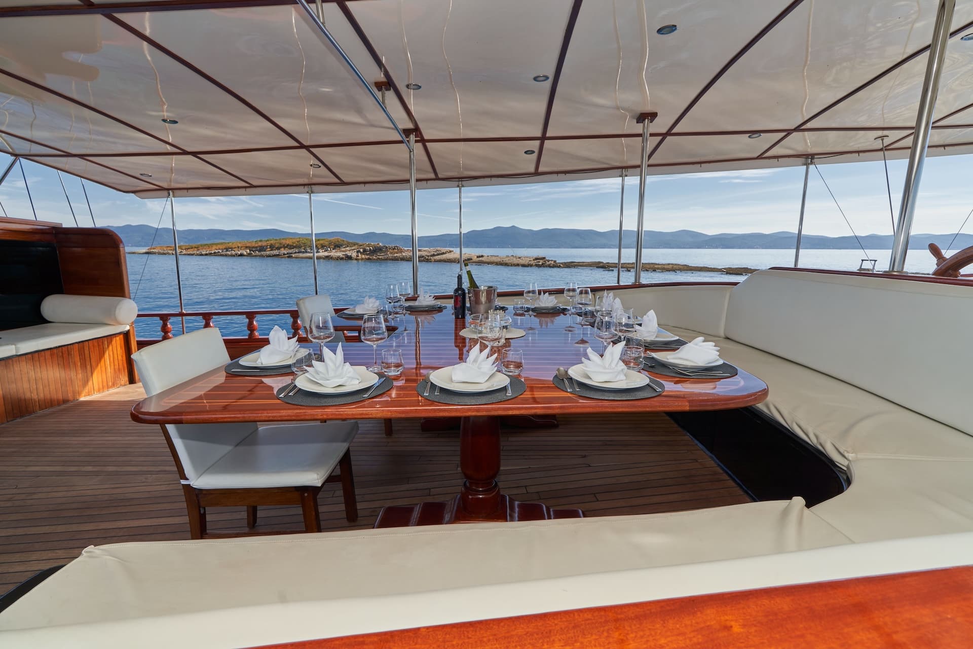 Outdoor dining table set on a yacht deck overlooking islands and mountains on the sea.