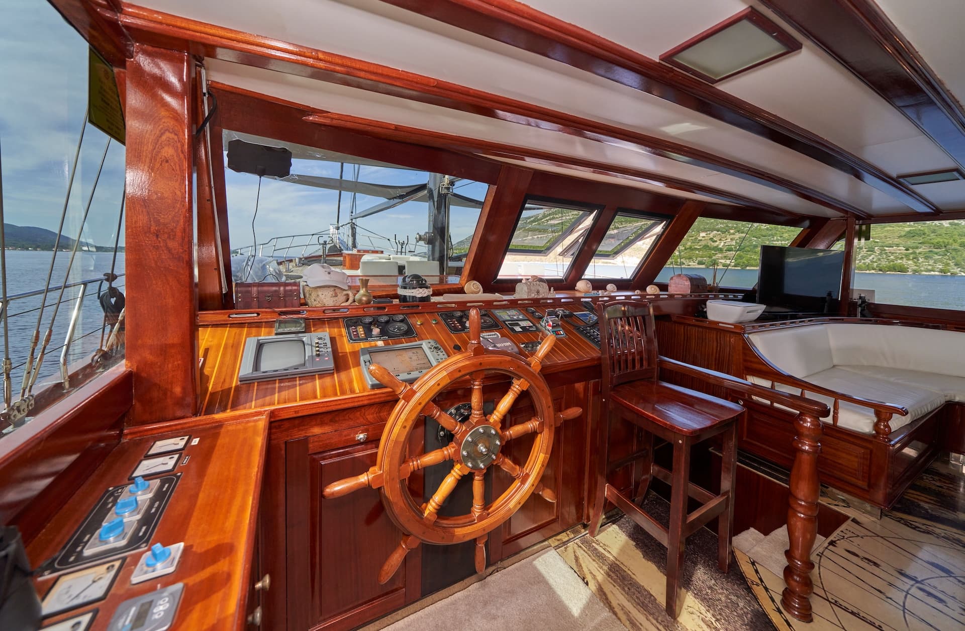 Yacht wheelhouse with polished wood, navigation screens, and view of green coastline.