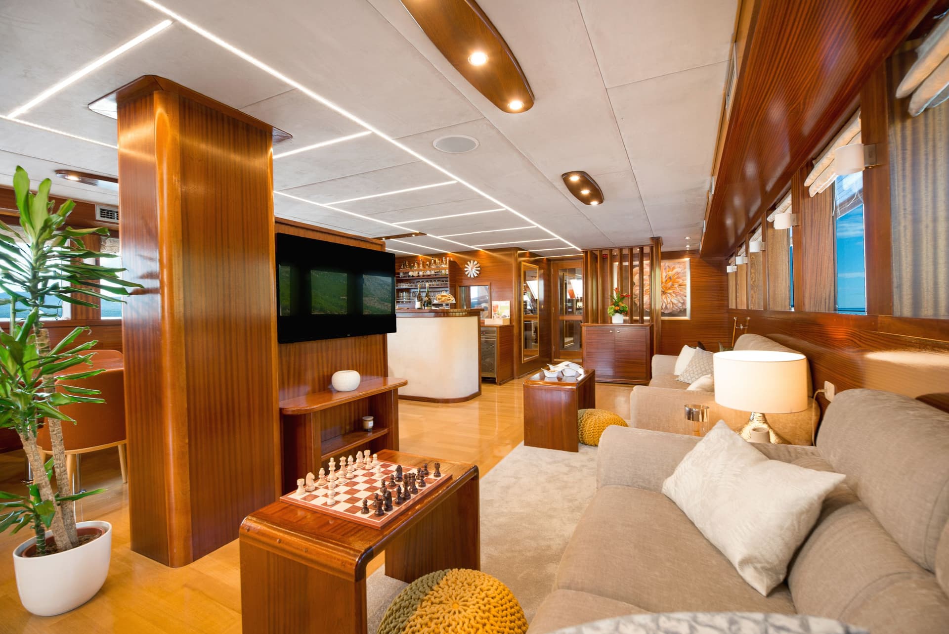 Luxurious yacht lounge with wood paneling, seating area, chessboard, and bar area.