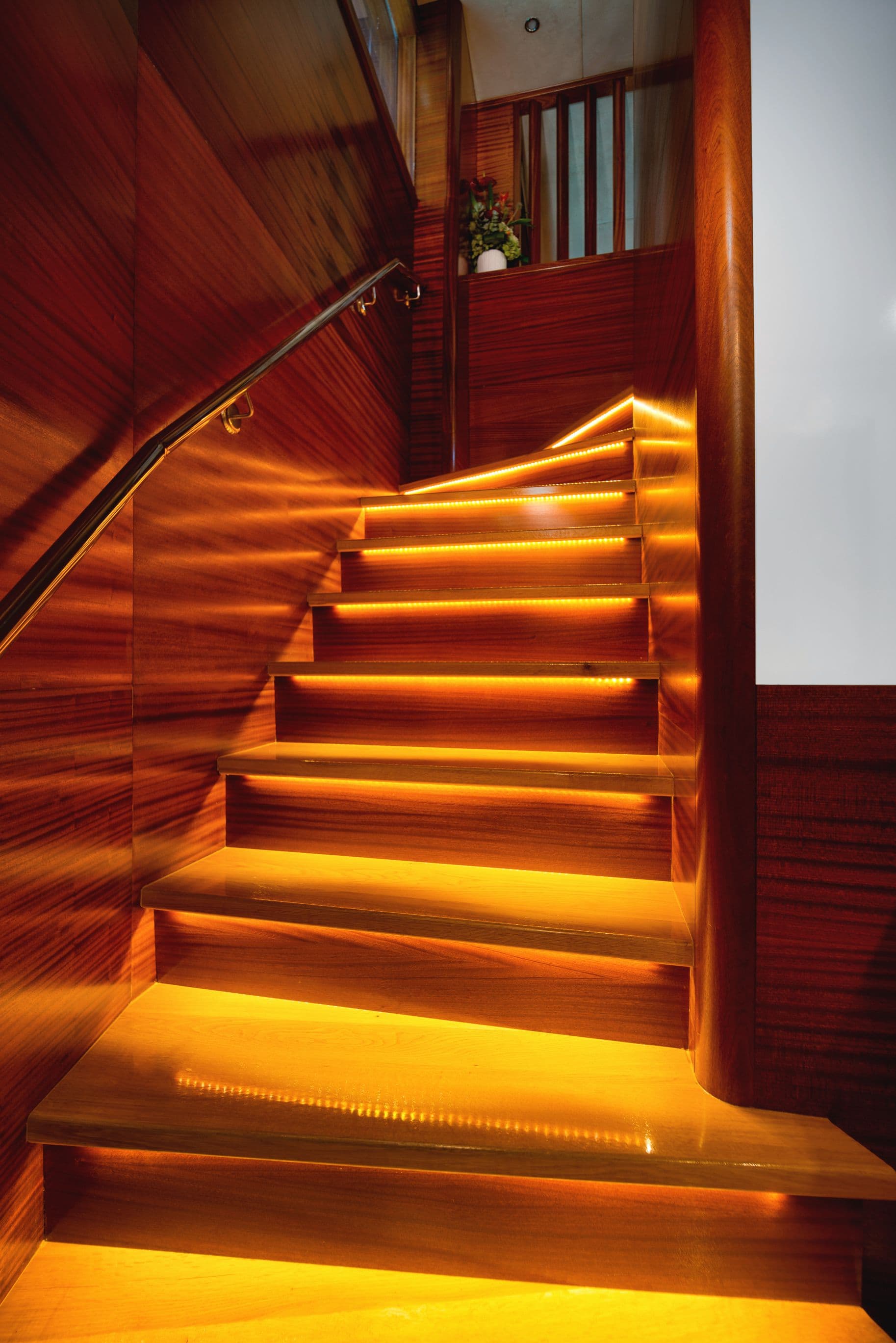 Wooden staircase with warm under-tread LED lighting in interior space, possibly a yacht.