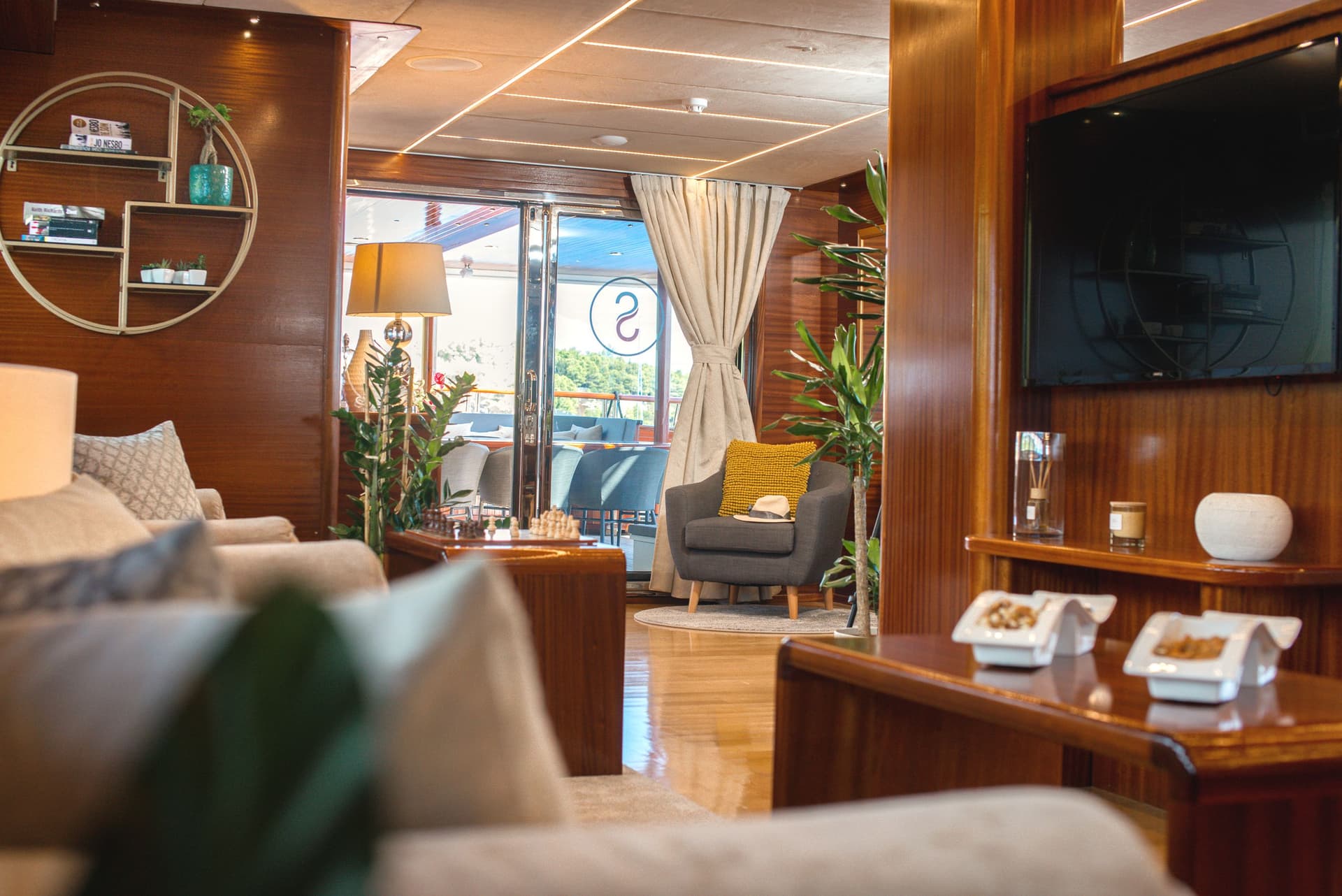 Luxury yacht interior lounge with wood paneling, seating, and view of the deck.