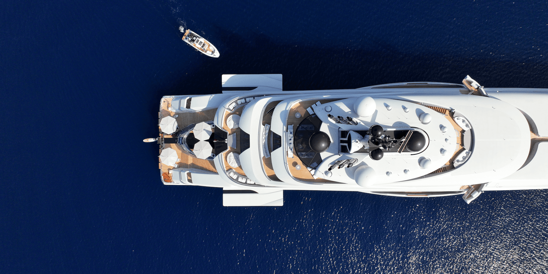 Aerial view of a large white luxury yacht on deep blue water near a small tender boat.