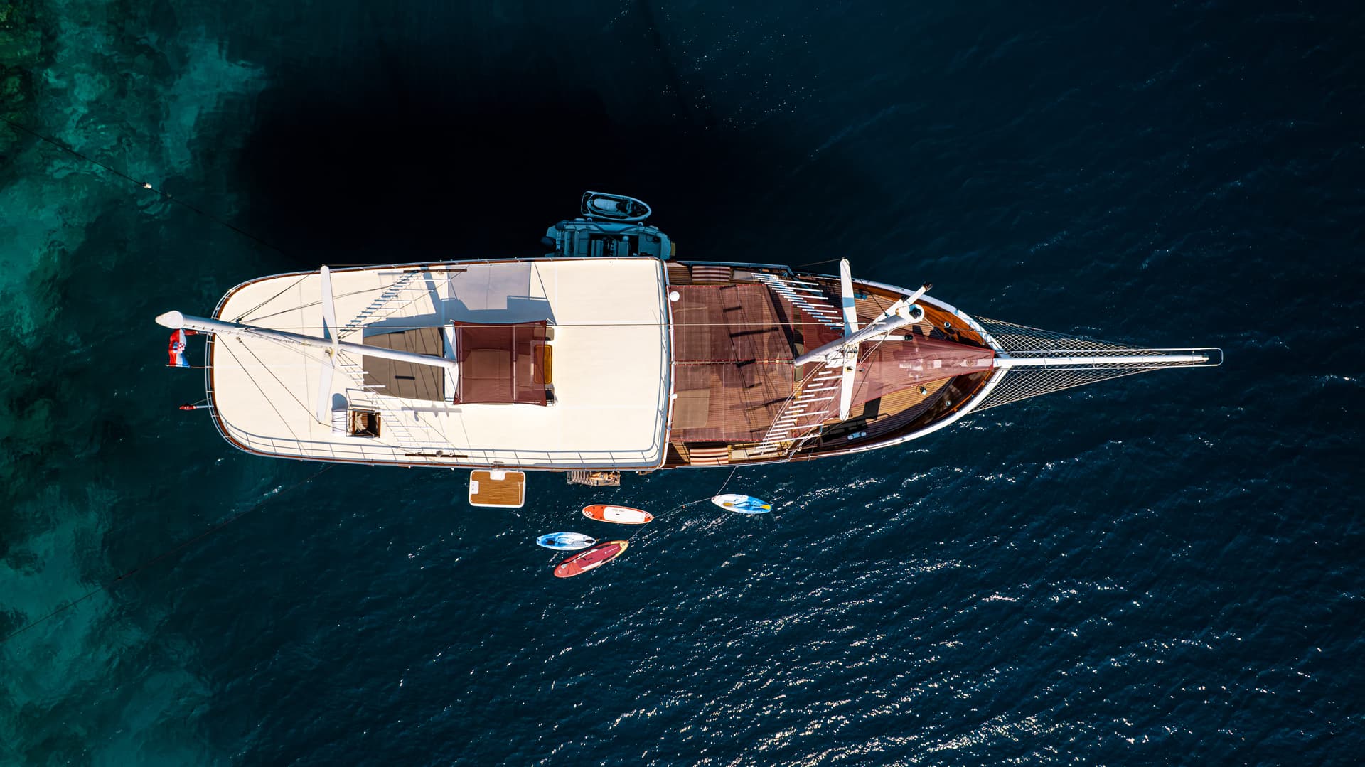 Aerial view of a large wooden boat anchored near turquoise water with paddleboards floating nearby.