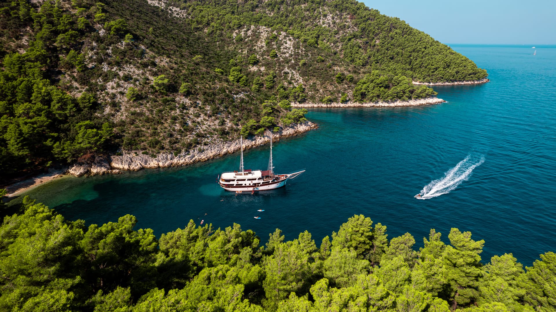 Large wooden boat anchored in cove with turquoise water near forested cliffs