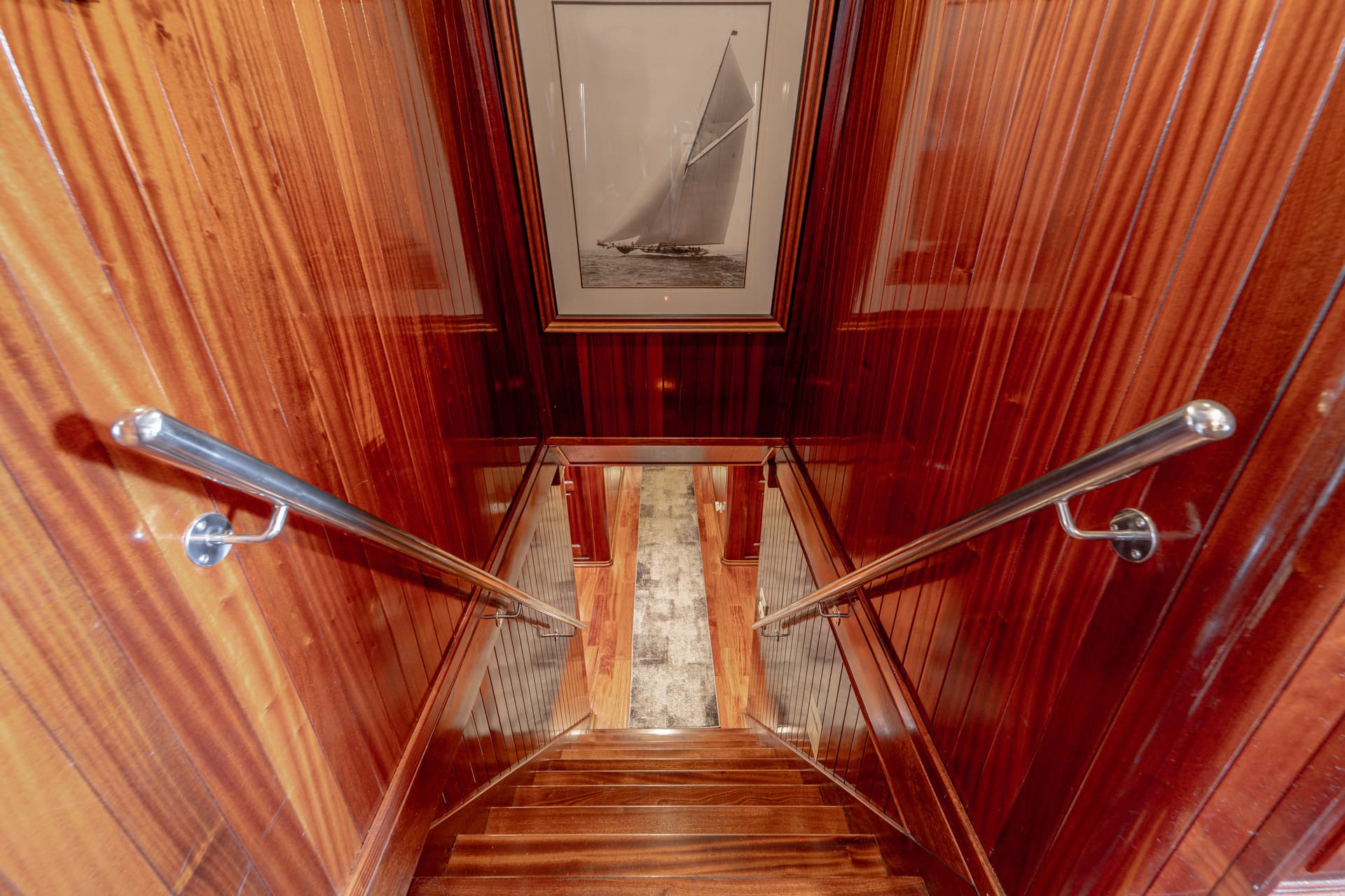 Wooden staircase with stainless steel railings leading down, framed sailboat art above.