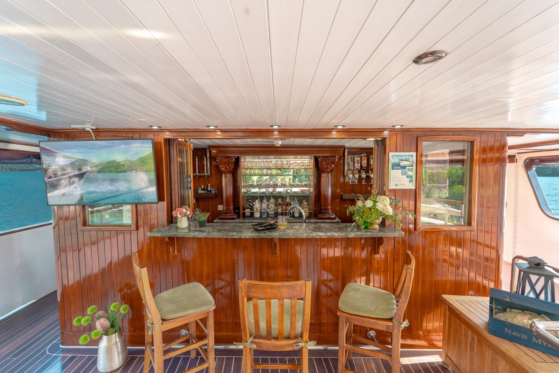Bar area with polished wood and marble counter on a boat, blue water visible outside.