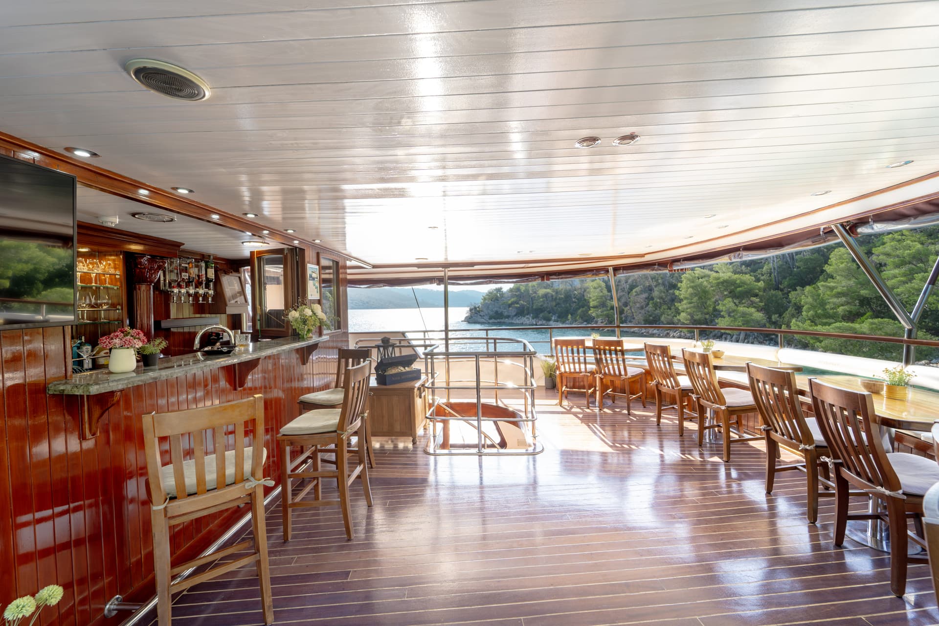 Boat bar and dining area with wooden floors overlooking a forested coastline.