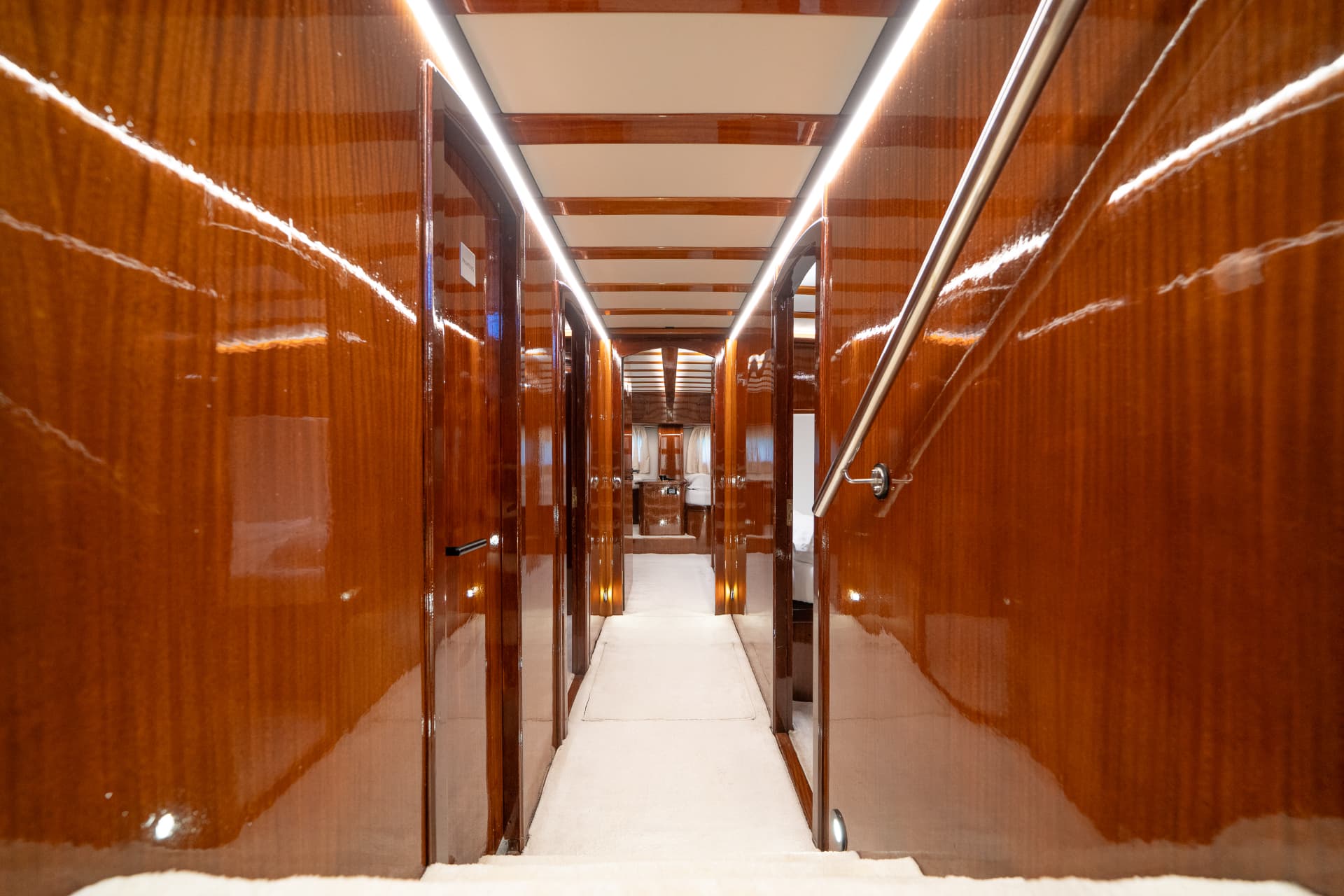 Yacht interior hallway with glossy wood paneling, white carpet, and recessed lighting leading to cabins.