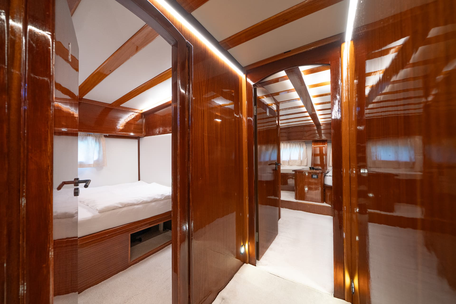 Interior cabin hallway with glossy wood paneling and white carpet, showing a berth.