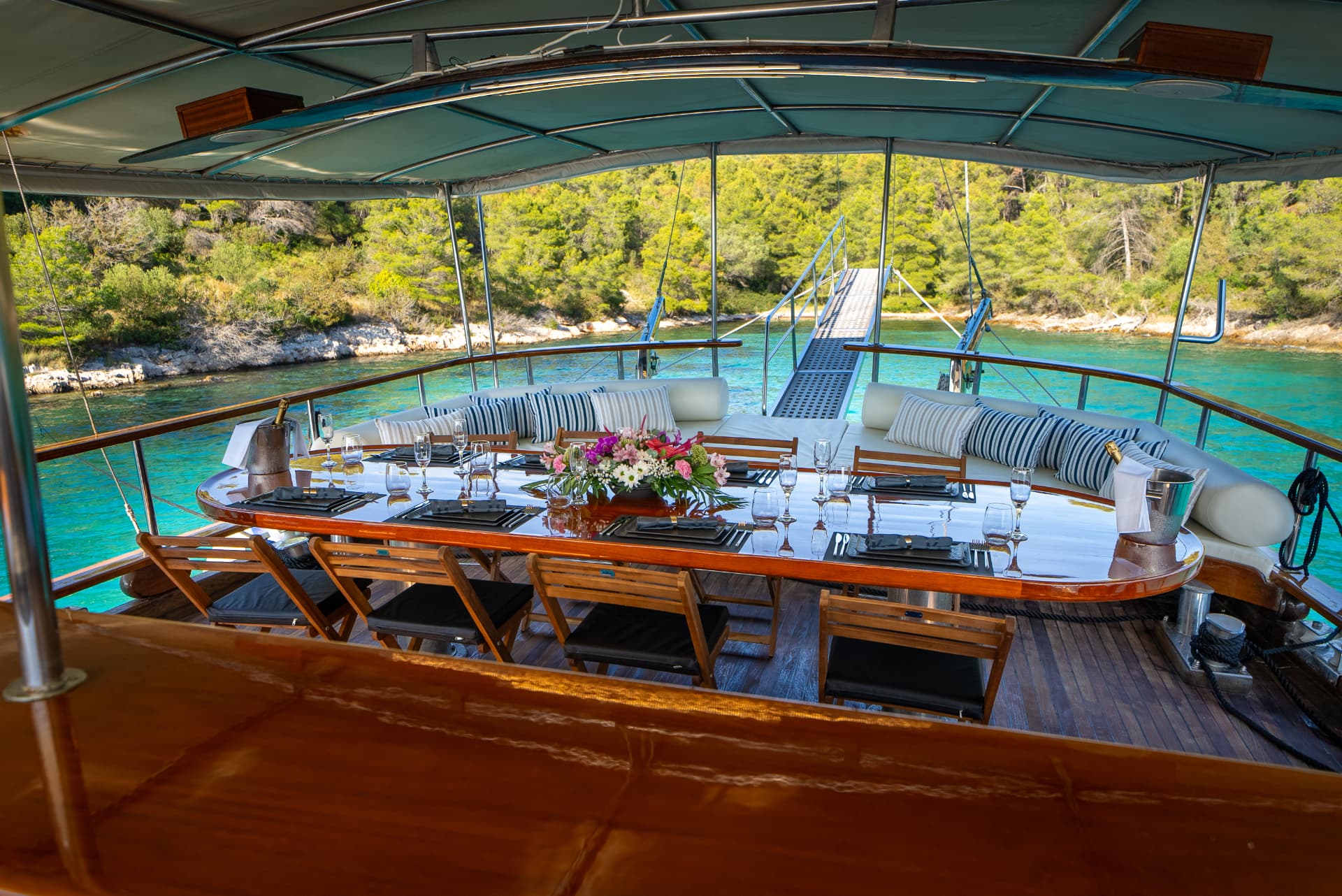 Dining setup on a yacht deck overlooking turquoise water and a forested coastline.