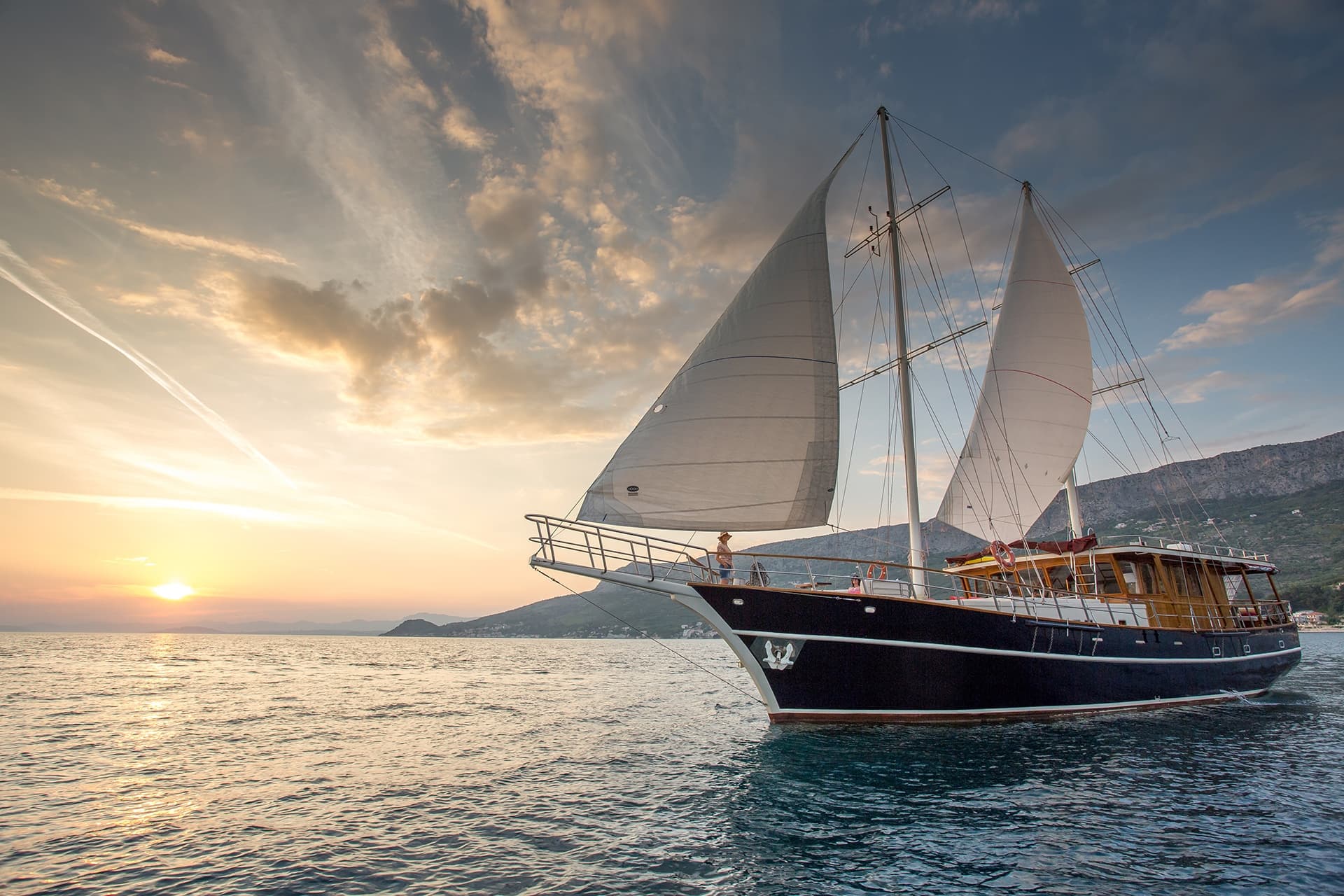 Large sailboat with sails up on the sea near mountains at sunset