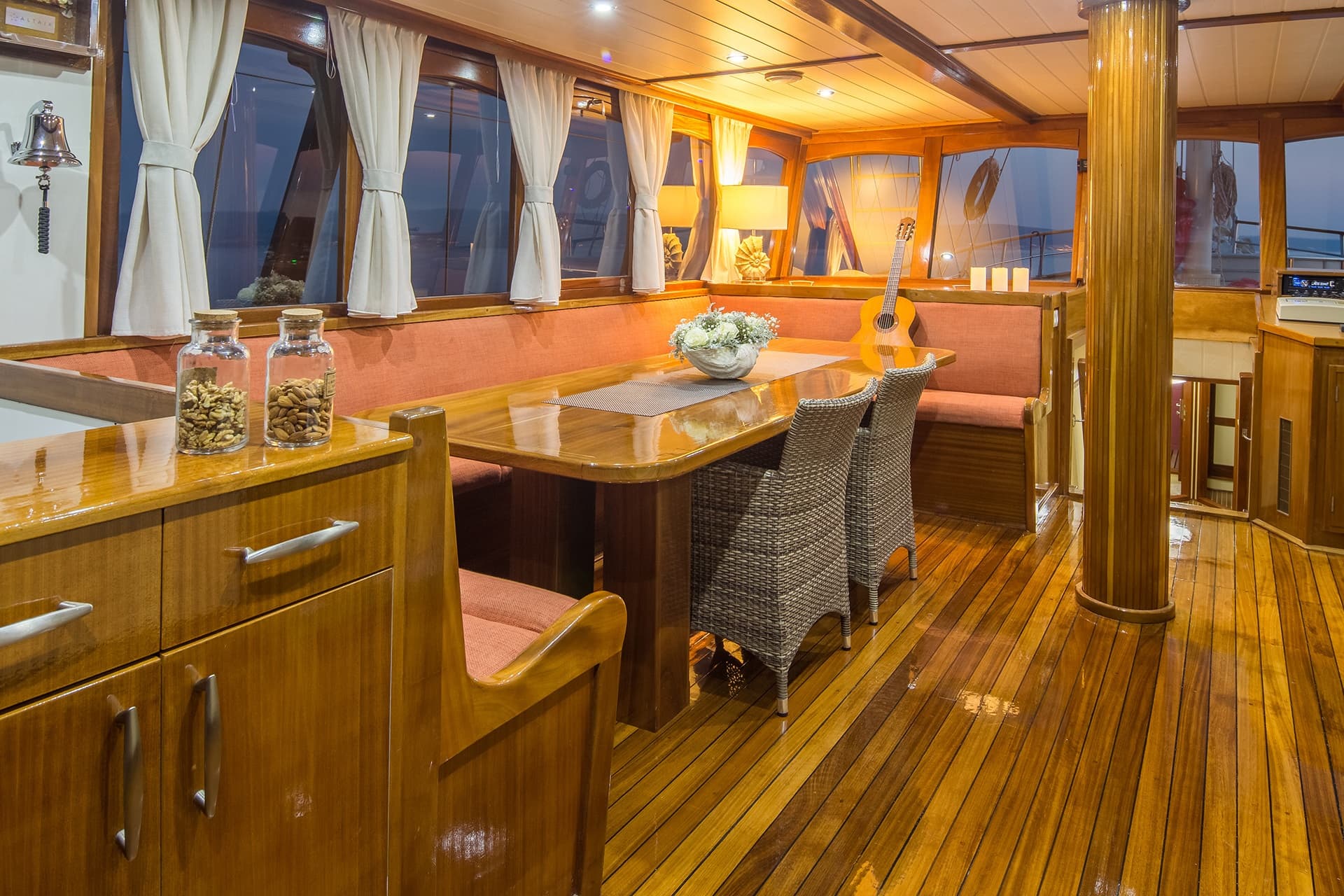 Dining area inside a yacht with polished wood, built-in seating, and views of the sea.